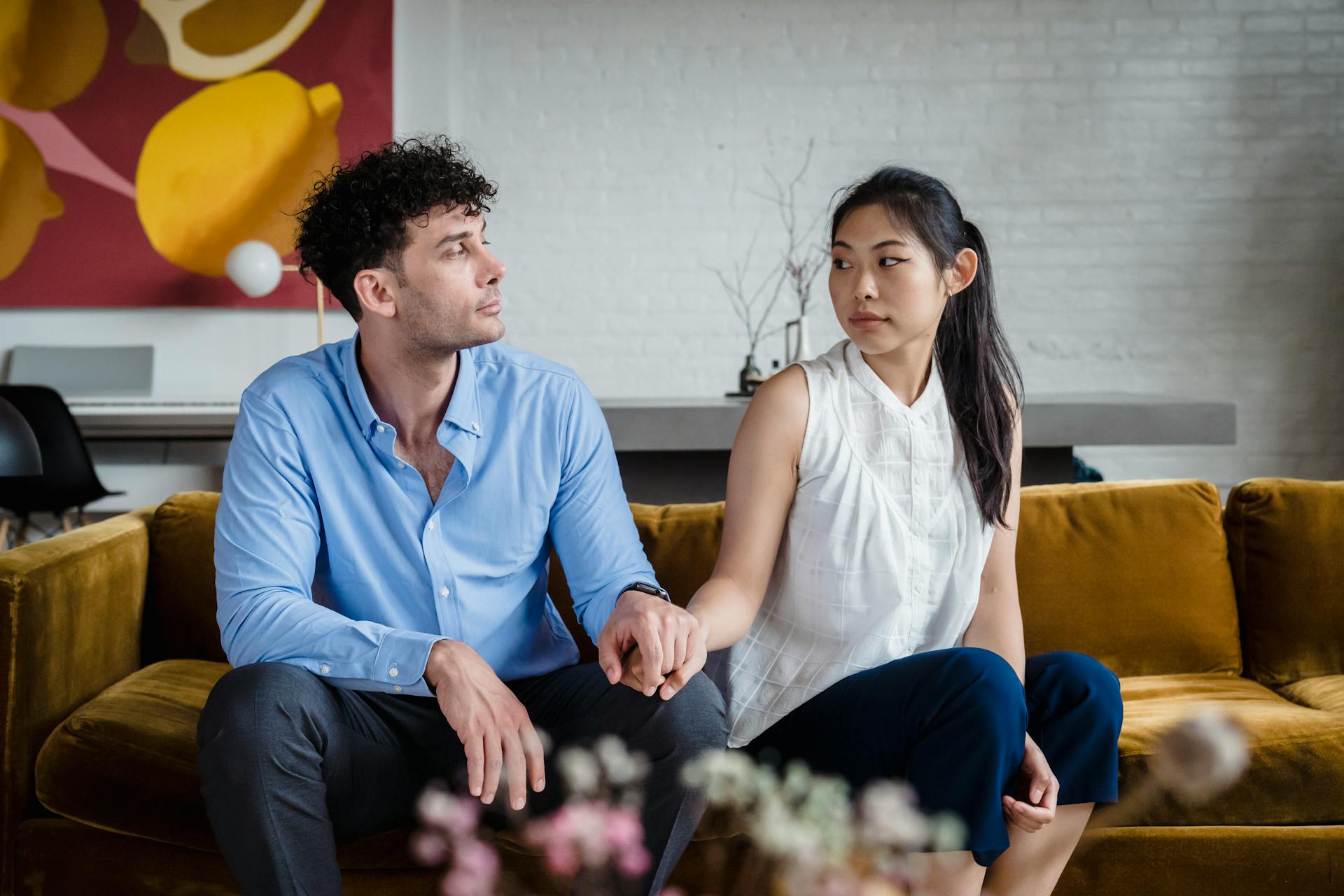 Un couple inquiet se tenant par la main, assis sur un canapé | Source : Pexels