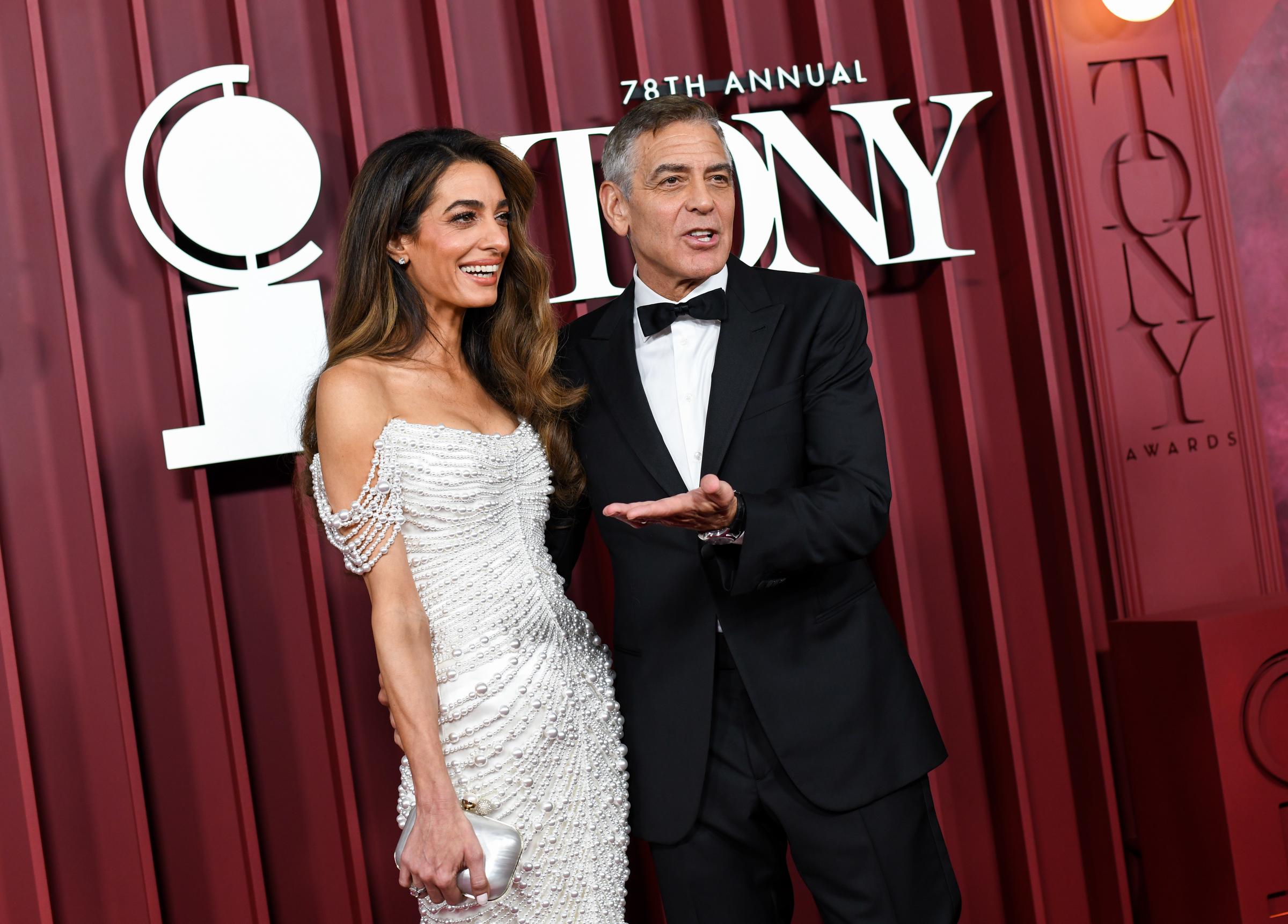 Amal et George Clooney partagent un échange léger alors qu'ils arrivent à la cérémonie des Tony Awards. George fait un geste au milieu d'une phrase tandis qu'Amal rit, ajoutant une énergie candide au tapis rouge.