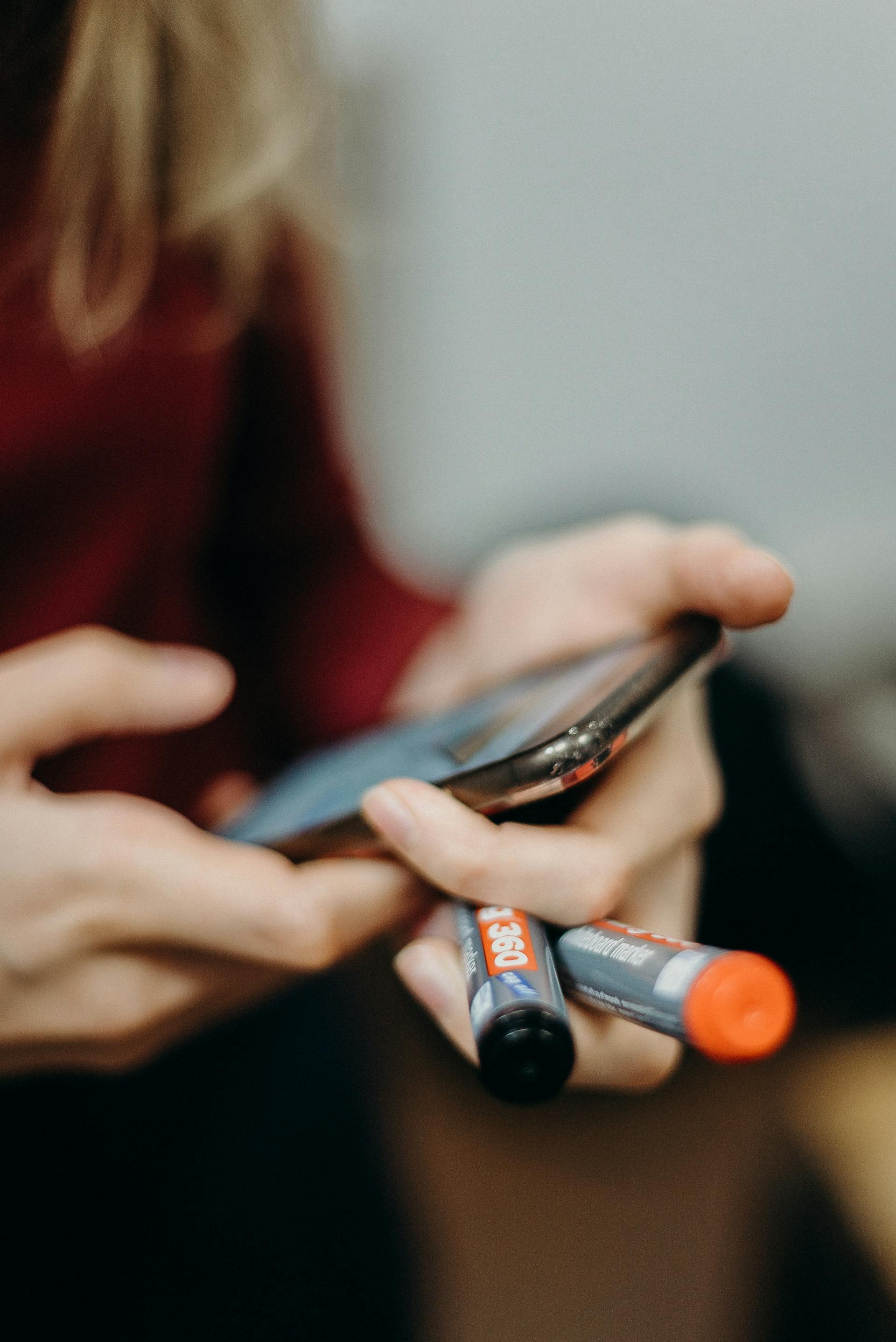Une femme tenant un smartphone et deux marqueurs | Source : Pexels
