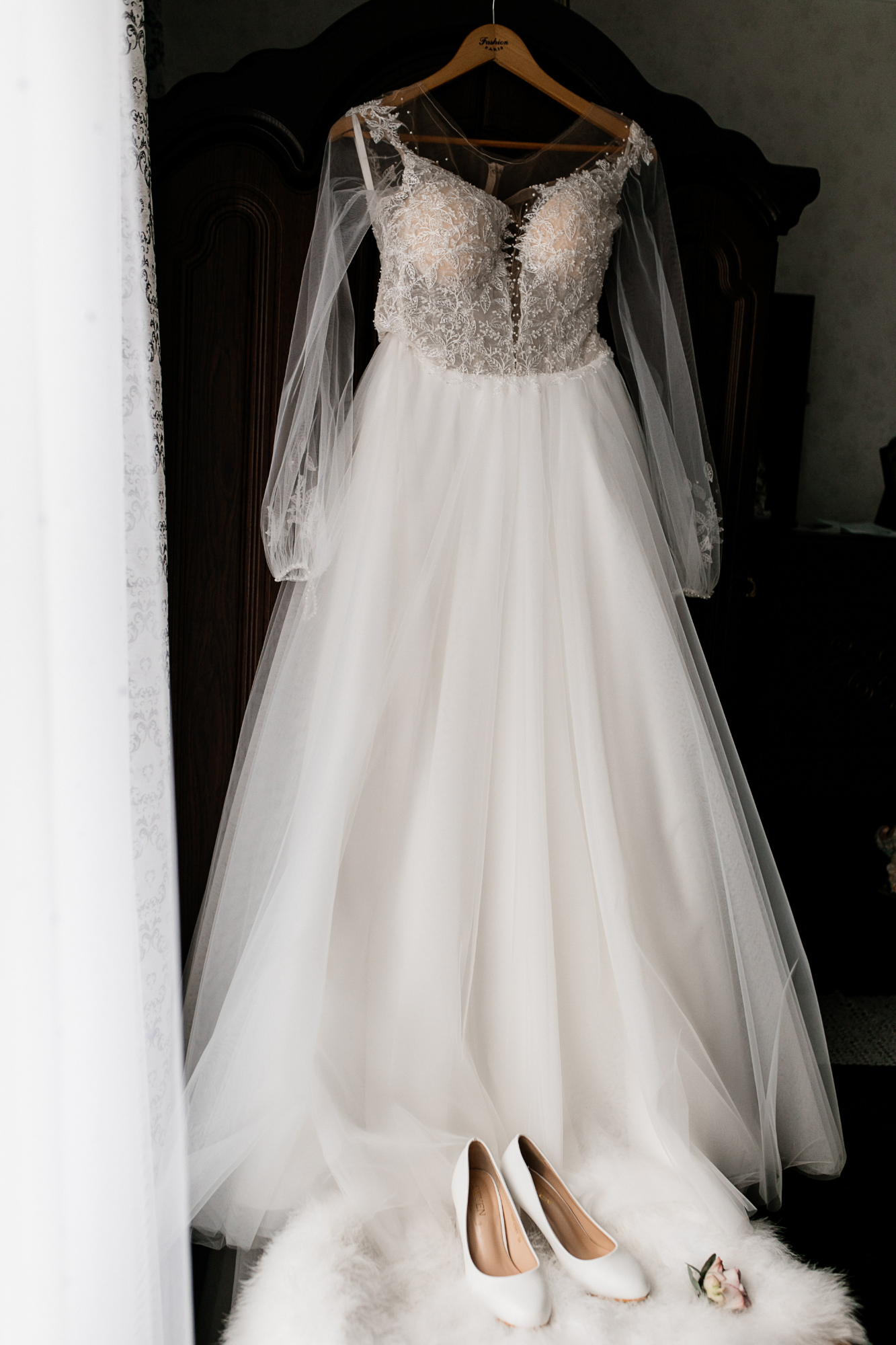 Une robe de mariée sur un cintre et des talons blancs posés sur un pouf en fourrure | Source : Freepik