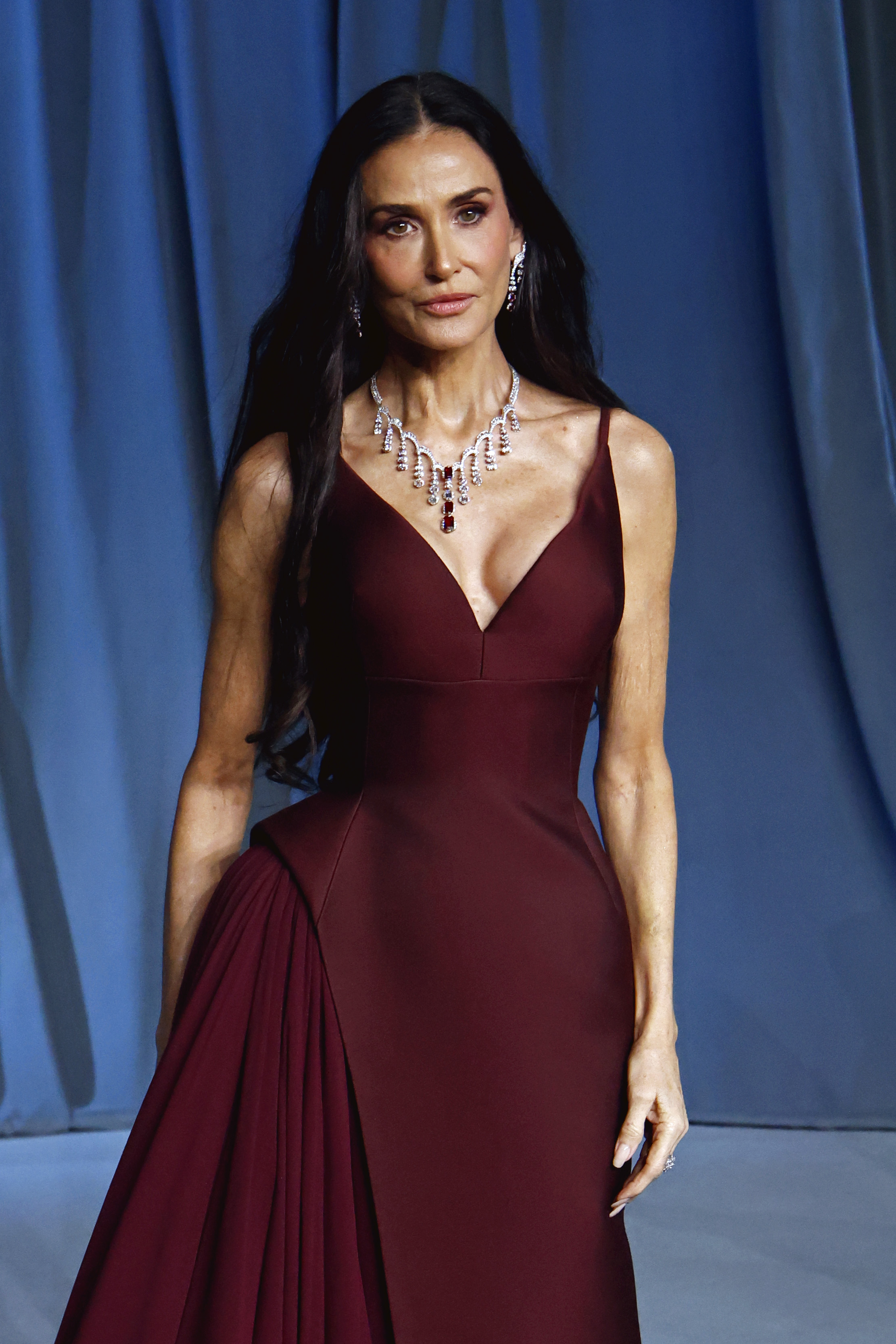 Avec sa présence féroce et sculpturale, Demi Moore attire tous les regards dans une robe structurée couleur bordeaux, mettant en valeur des plis audacieux et des bijoux éblouissants.