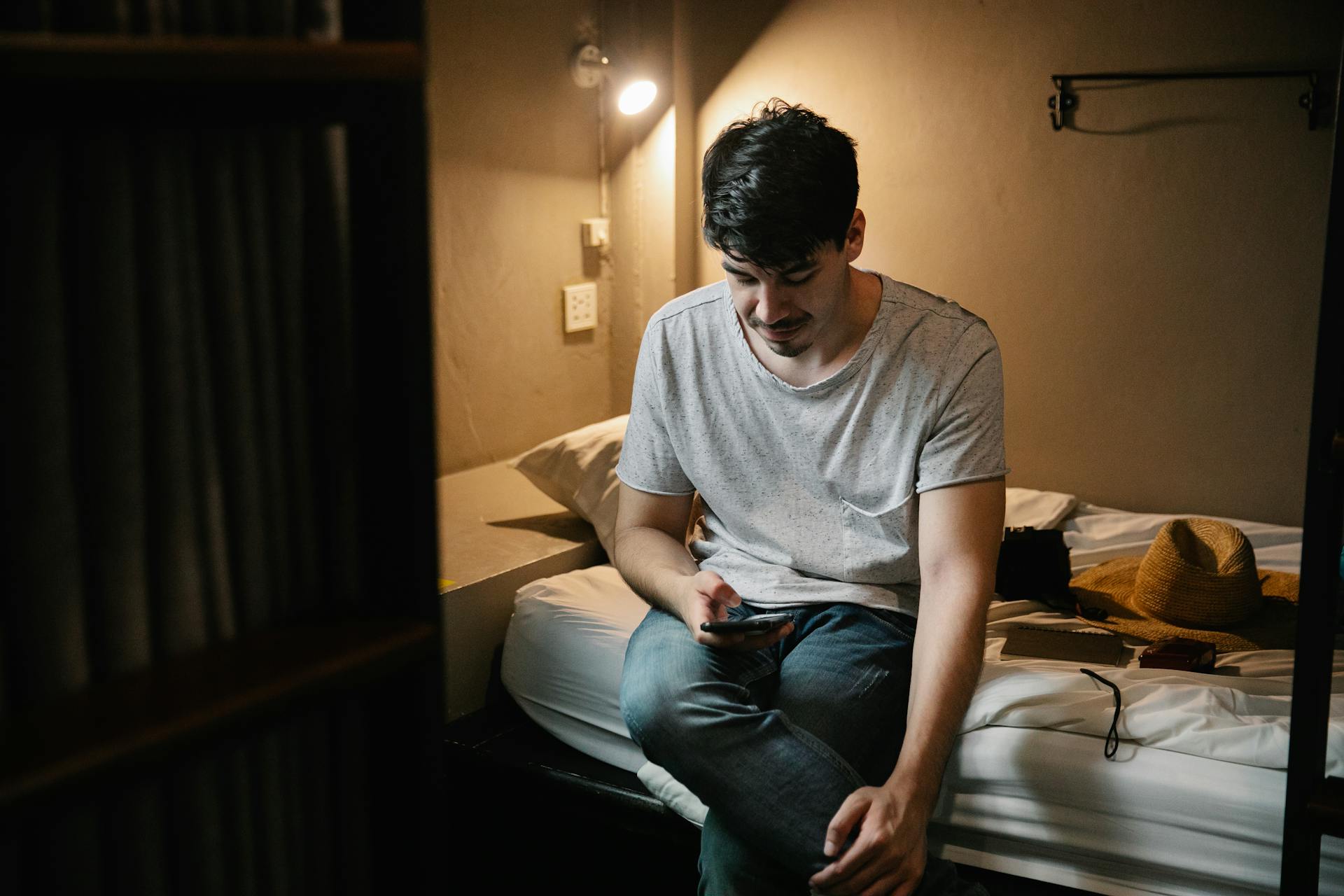 Un homme assis sur le lit et utilisant son téléphone | Source : Pexels