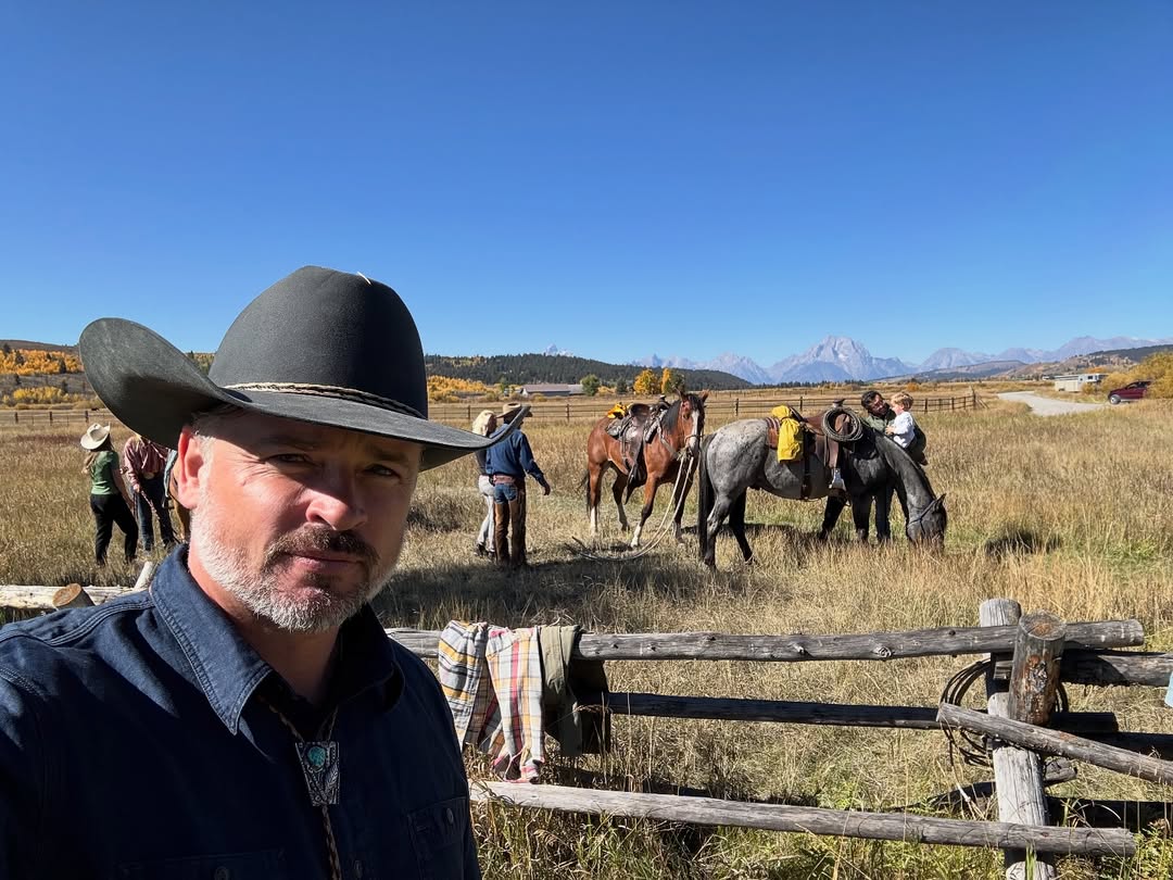 Tom Welling posant dans un ranch avec des personnes et des chevaux en arrière-plan dans le Wyoming, le 27 septembre 2025 | Source : Instagram/tomwelling