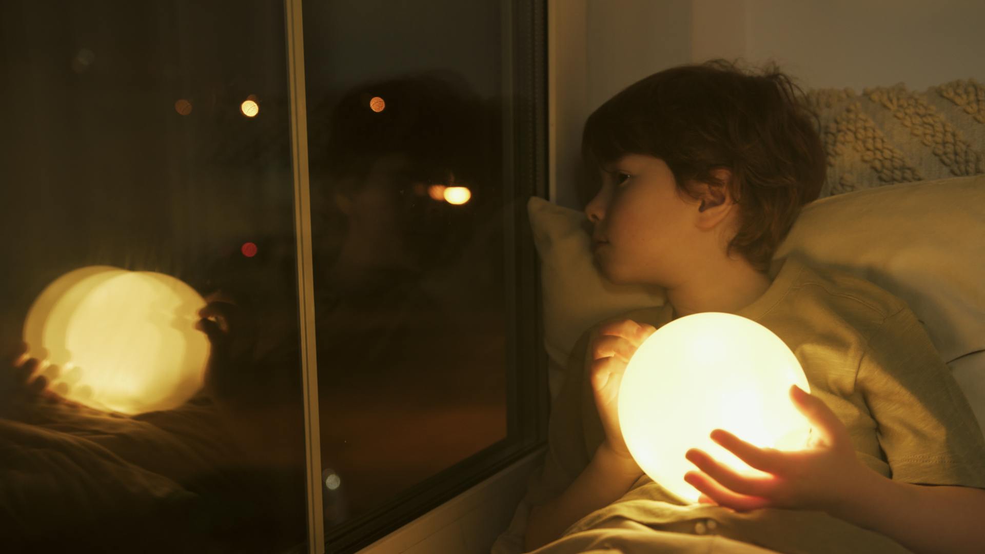 Un jeune garçon tenant une boule de lumière et regardant par la fenêtre | Source : Pexels