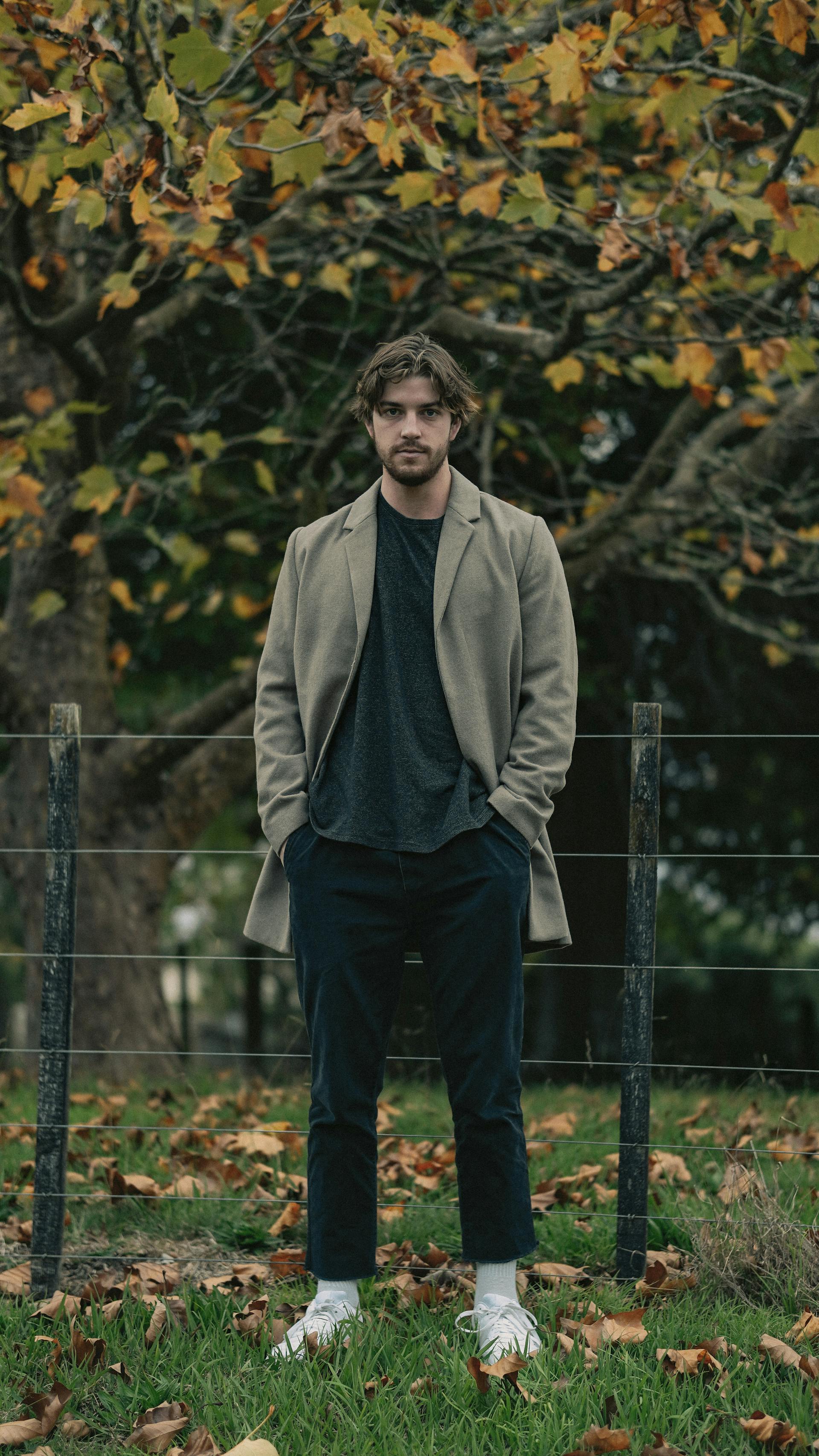 Un homme vêtu d'un manteau marron se tenant à côté d'une clôture en bois | Source : Pexels