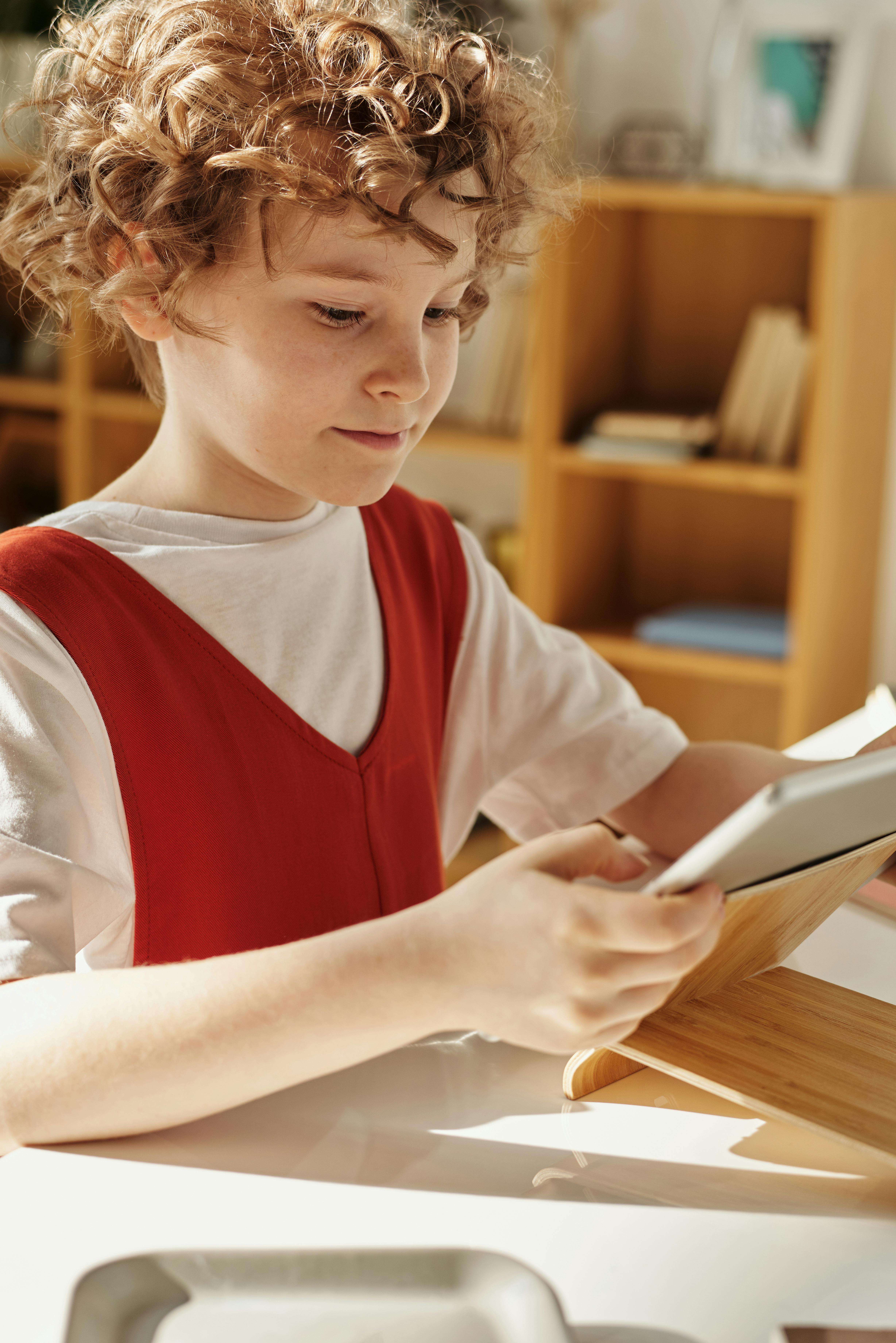 Un enfant utilisant une tablette posée sur un support en bois | Source : Pexels