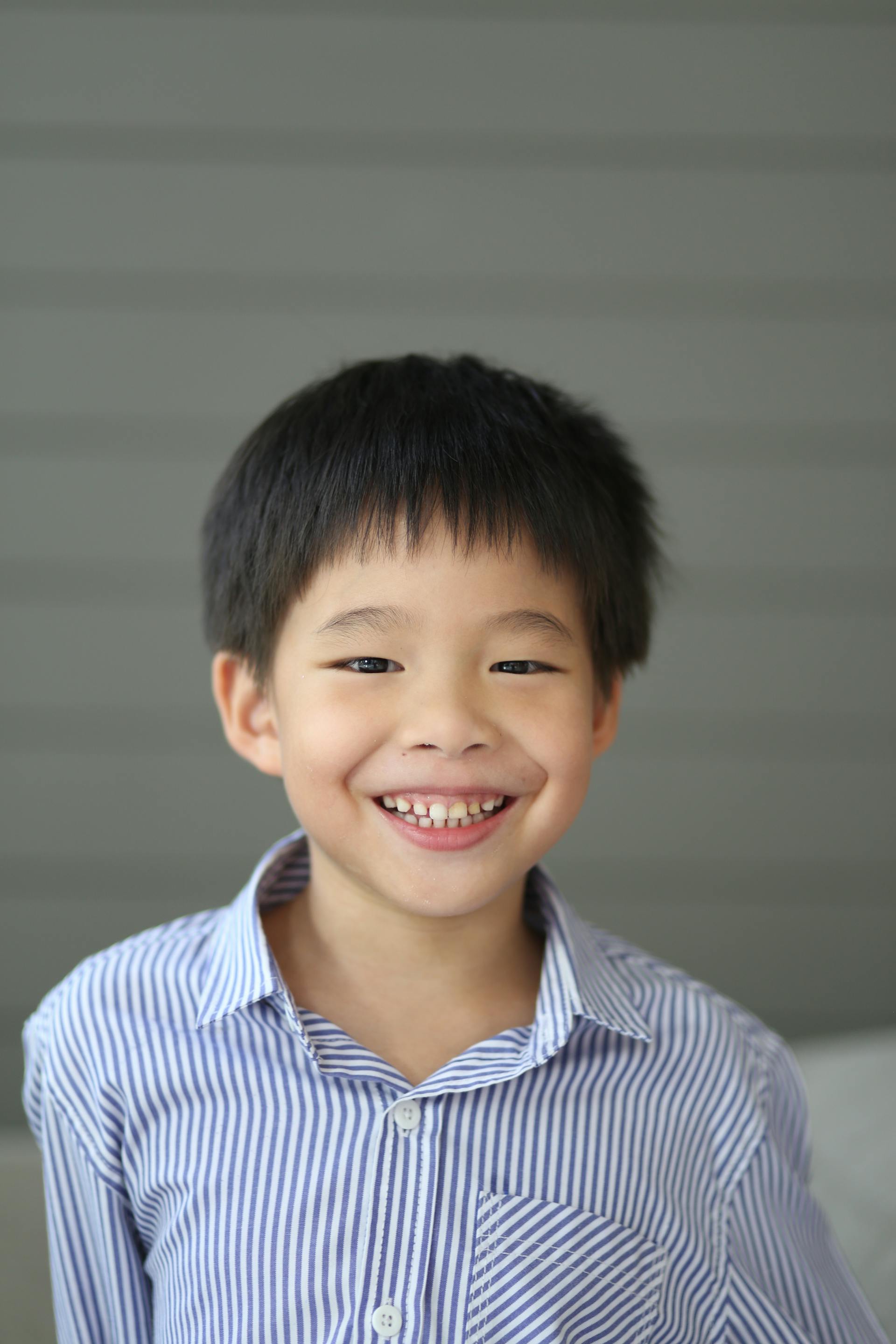 Un jeune garçon aux cheveux noirs courts souriant largement tout en portant une chemise rayée | Source : Pexels