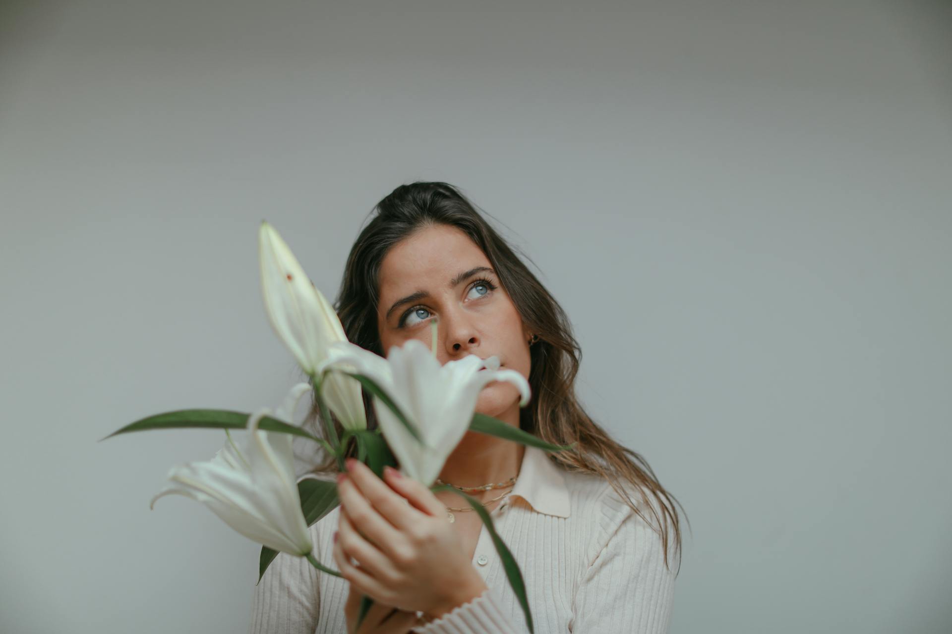 Une femme perdue dans ses pensées alors qu'elle tient des lys blancs | Source : Pexels