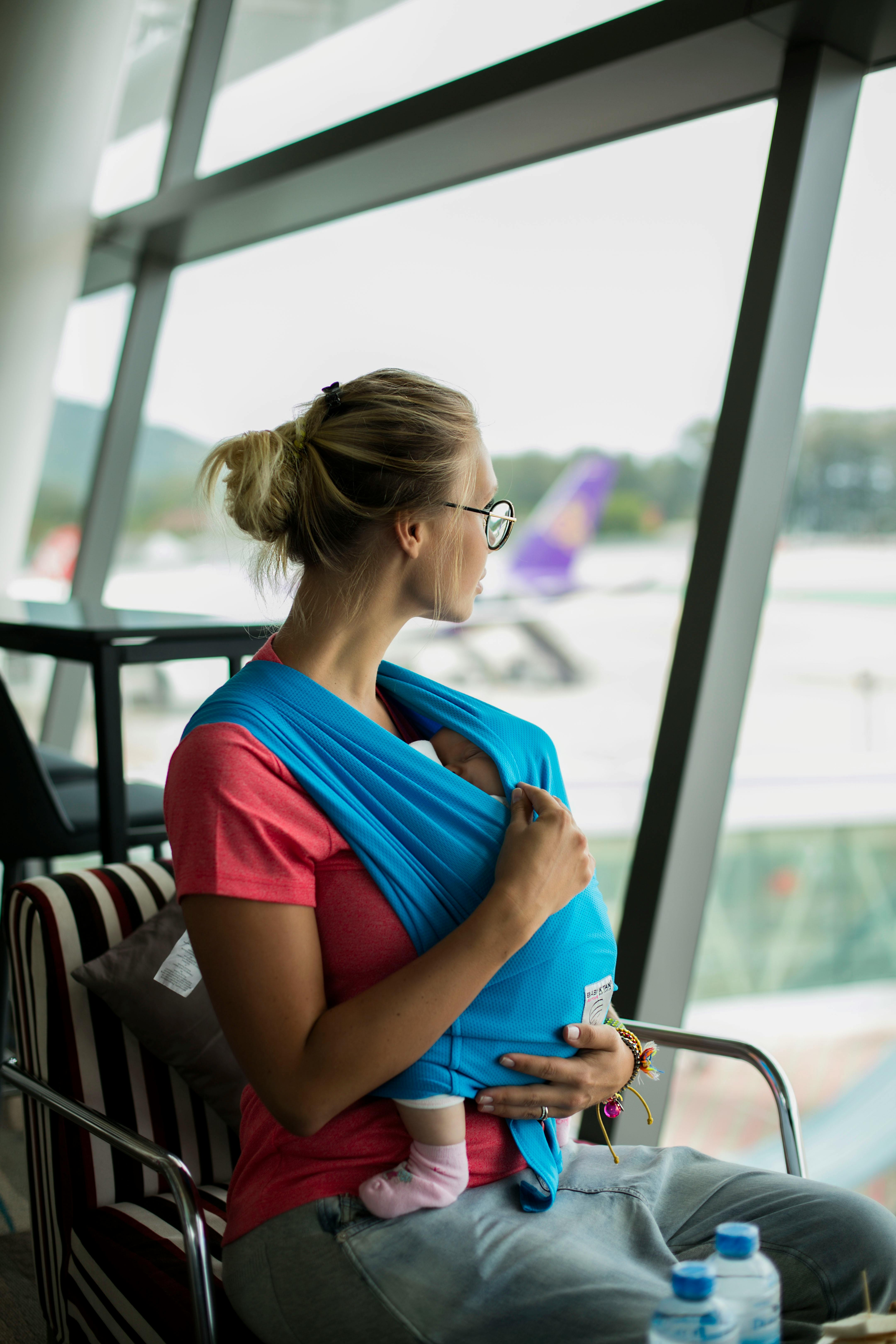Femme blonde avec un bébé regardant par la fenêtre d'un aéroport | Source : Pexels
