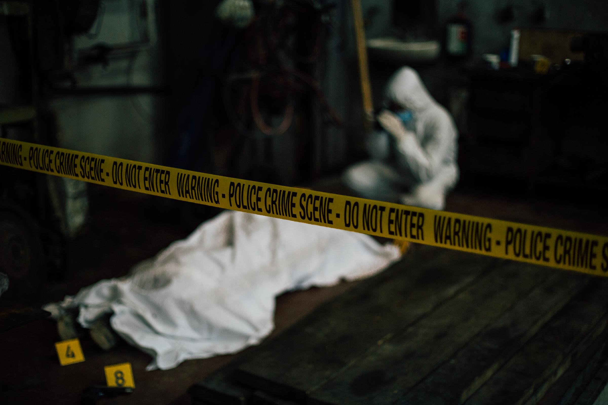 Image floue d'un enquêteur médico-légal sur une scène de crime - cadavre recouvert et preuves I Photo d'illustration I Source : Getty Images