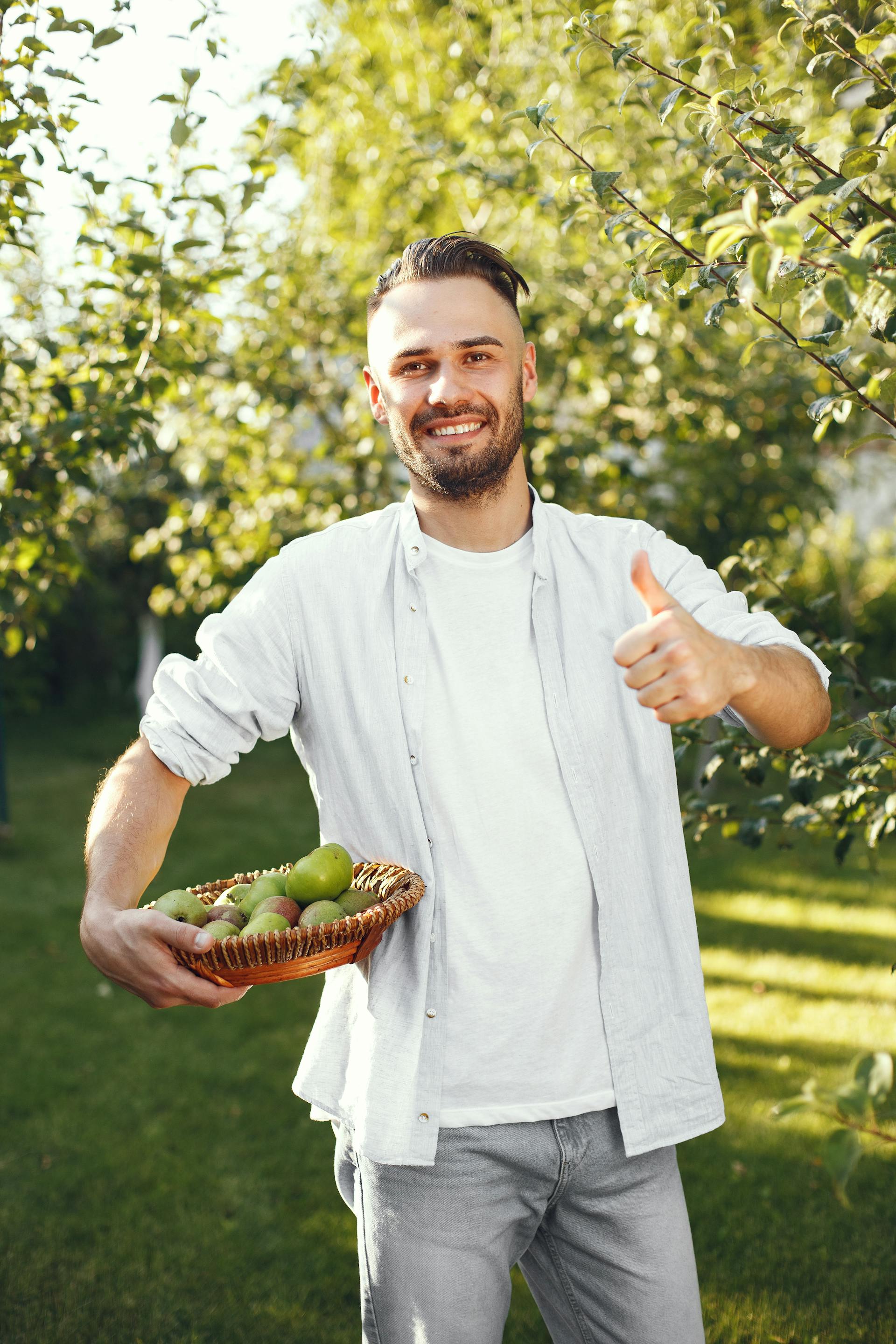 Un homme debout dans son jardin tenant une corbeille de fruits | Source : Pexels