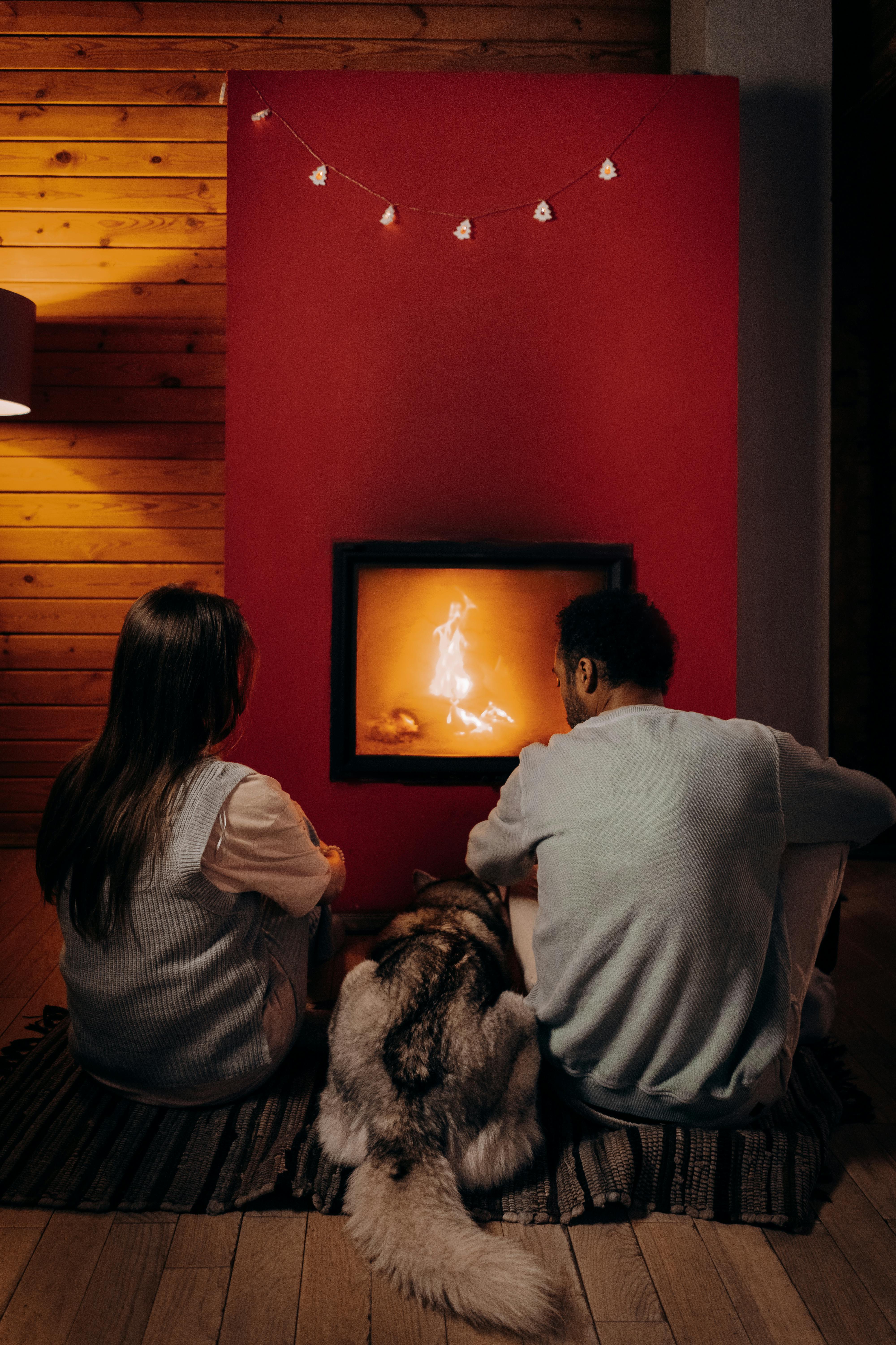 Un couple assis près d'une cheminée avec leur chien | Source : Pexels