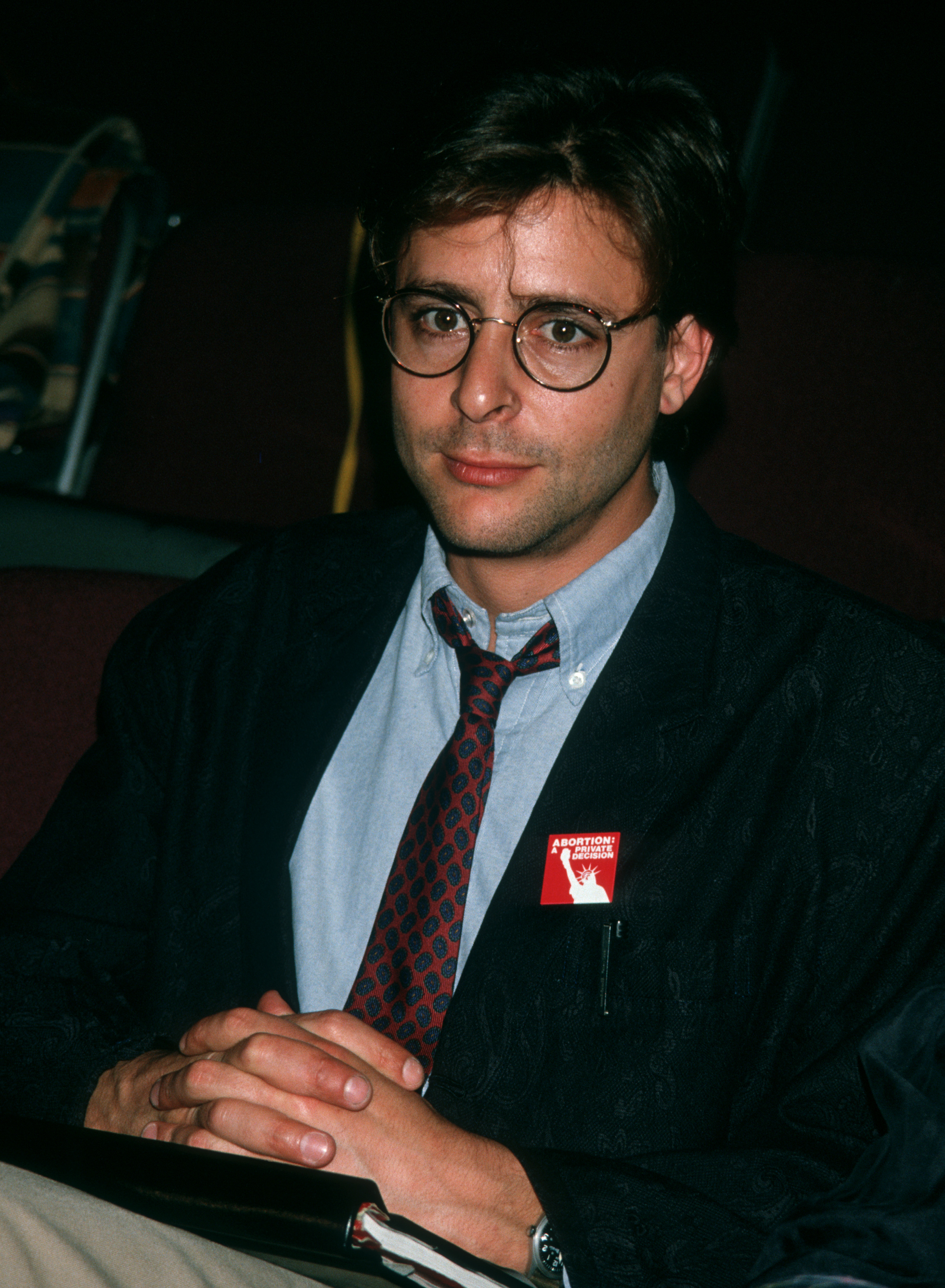 Assis, les mains jointes, lors de la première répétition de la pièce de théâtre « Carnal Knowledge » au Kaufman Theater à New York, l'acteur associait des lunettes rondes à une cravate à motifs, avec un pin's militant sur le revers de son blazer. | Source: Getty Images