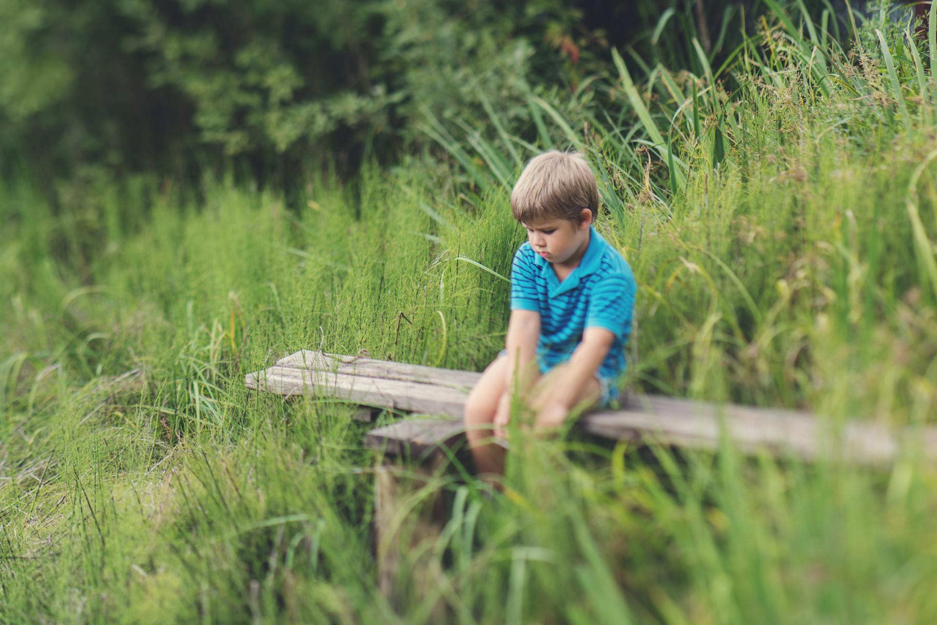 Un garçon vêtu d'un t-shirt bleu assis seul sur un banc en bois | Source : Pexels