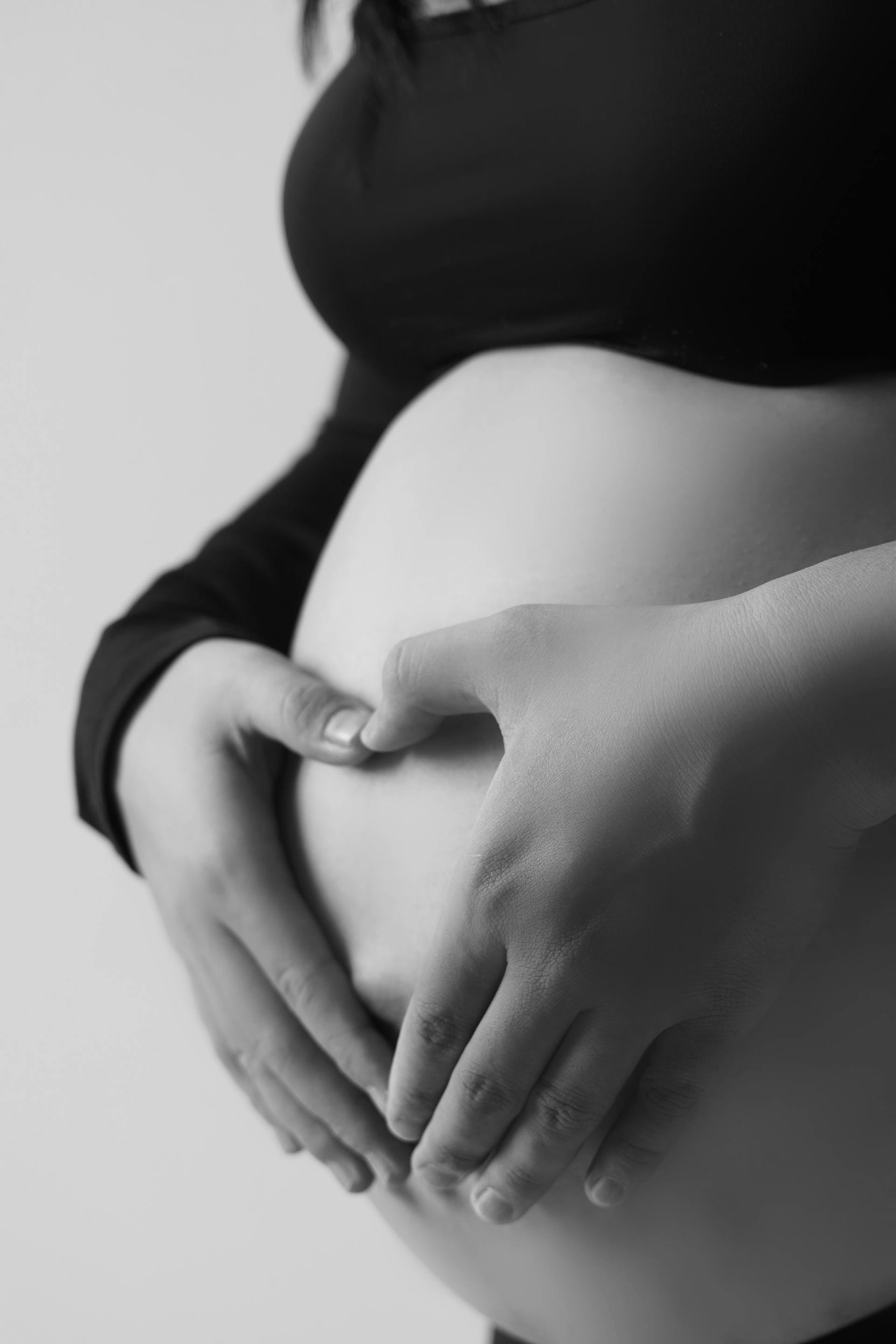 Photo en niveaux de gris d'un ventre de femme enceinte avec des mains formant un cœur | Source : Pexels