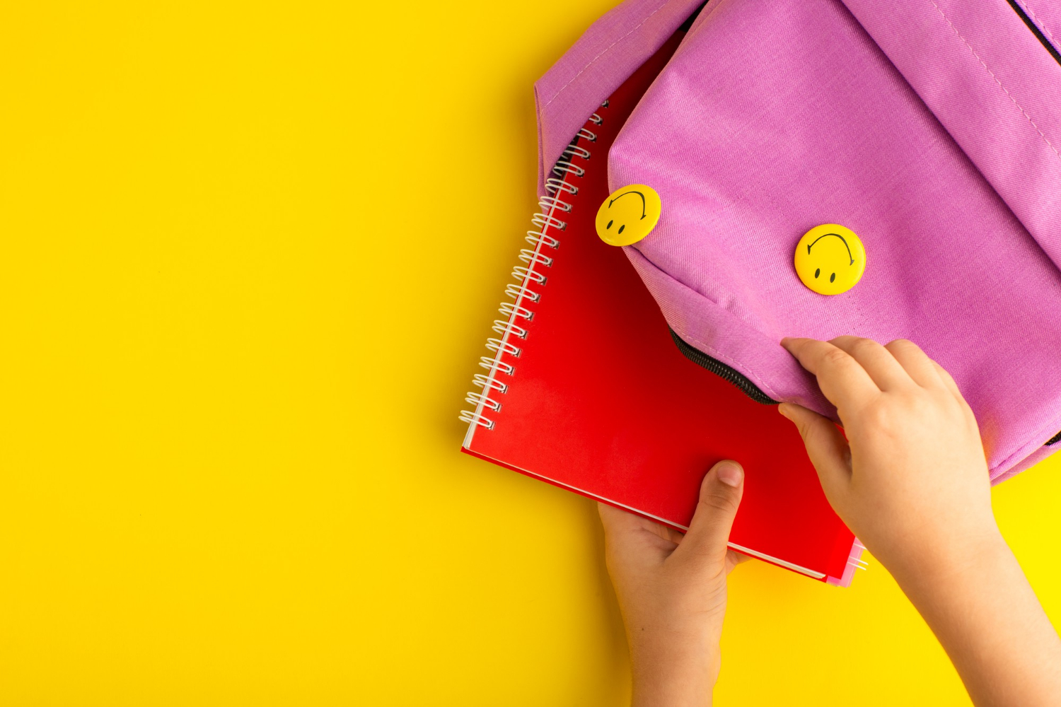 Gros plan sur un enfant qui met un cahier à l'intérieur d'un sac rose | Source : Freepik
