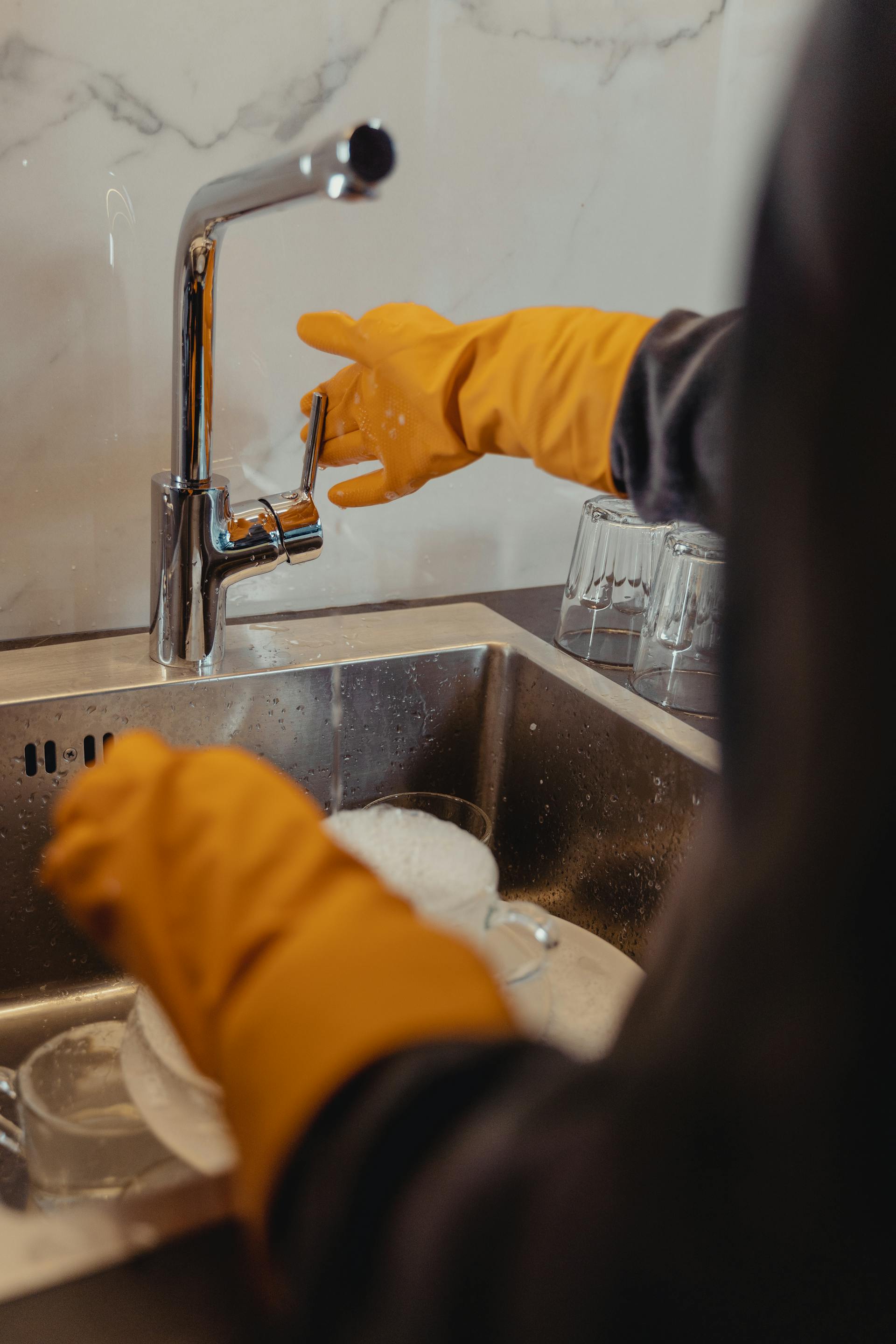 Une personne portant des gants jaunes en train de faire la vaisselle | Source : Pexels