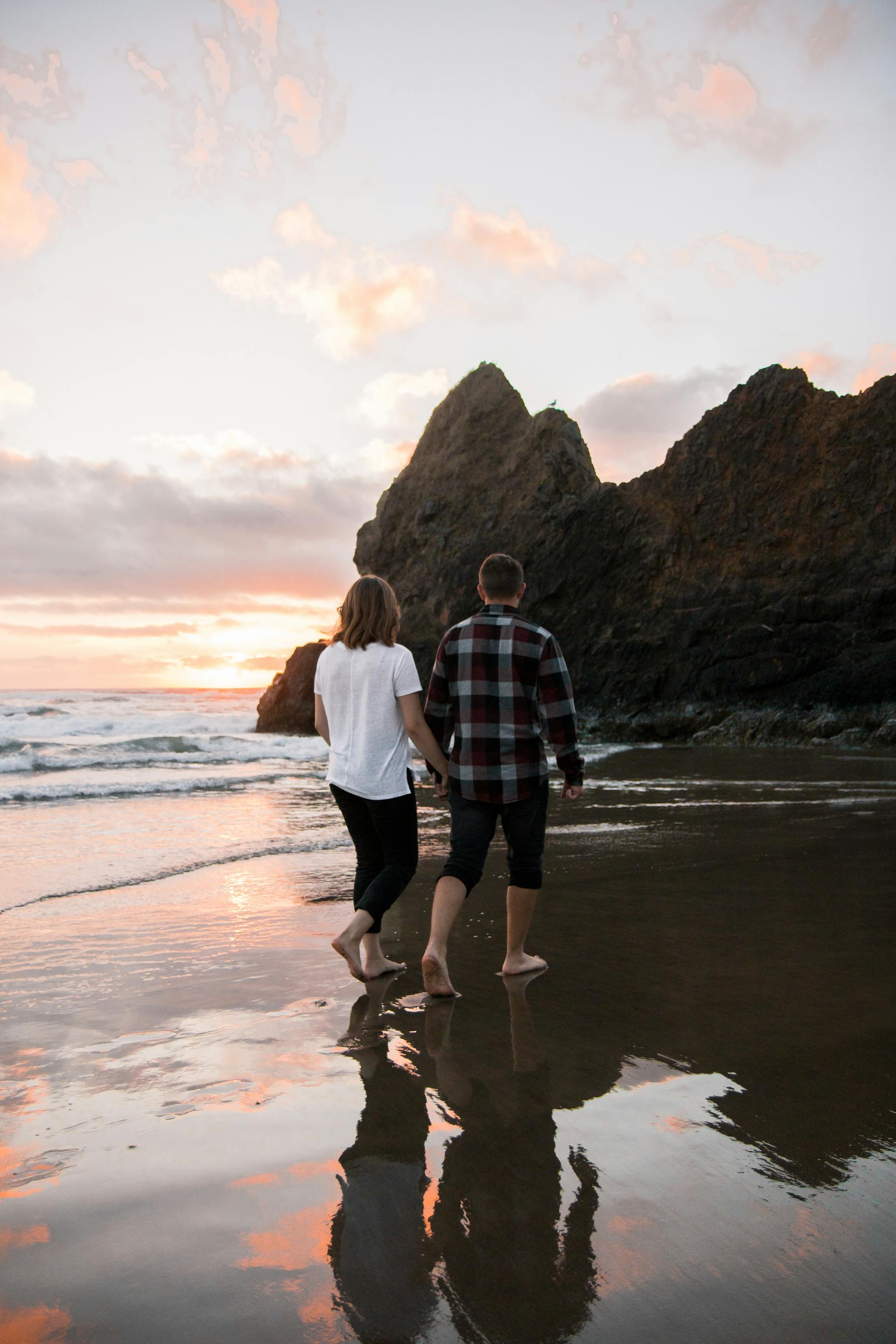 Un couple se tenant par la main tout en marchant pieds nus sur le rivage | Source : Pexels