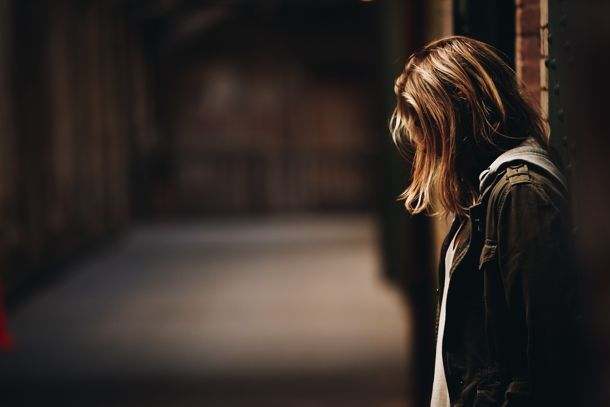 Une adolescente adossée au mur, regardant vers le bas dans un couloir | Source : Freepik