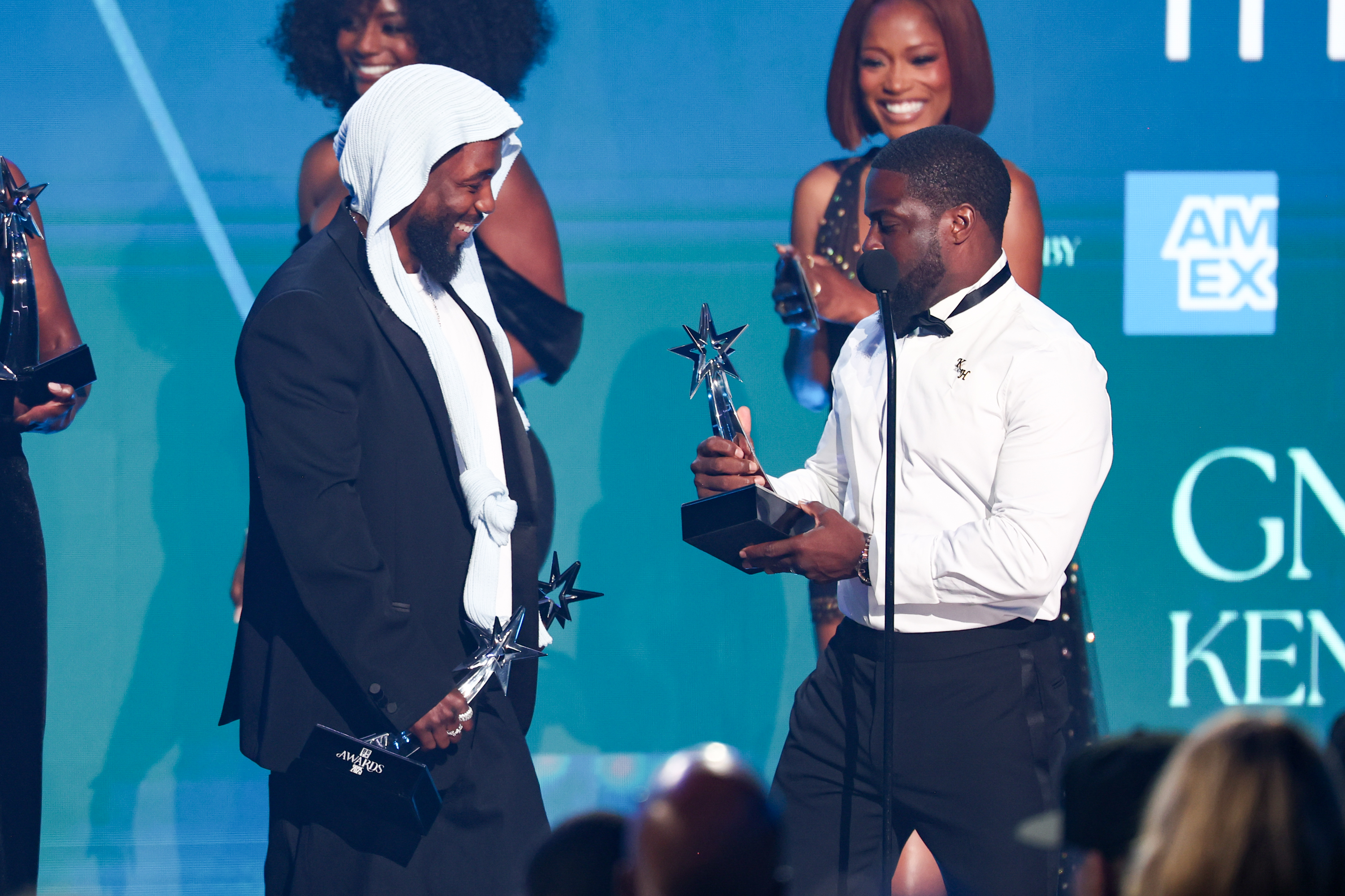 Kendrick Lamar sourit tandis que Kevin Hart lui remet un nouveau prix lors des BET Awards 2025. Les plaisanteries légères du duo ont ajouté une touche comique à la série de récompenses remportées par le rappeur au cours de la soirée.