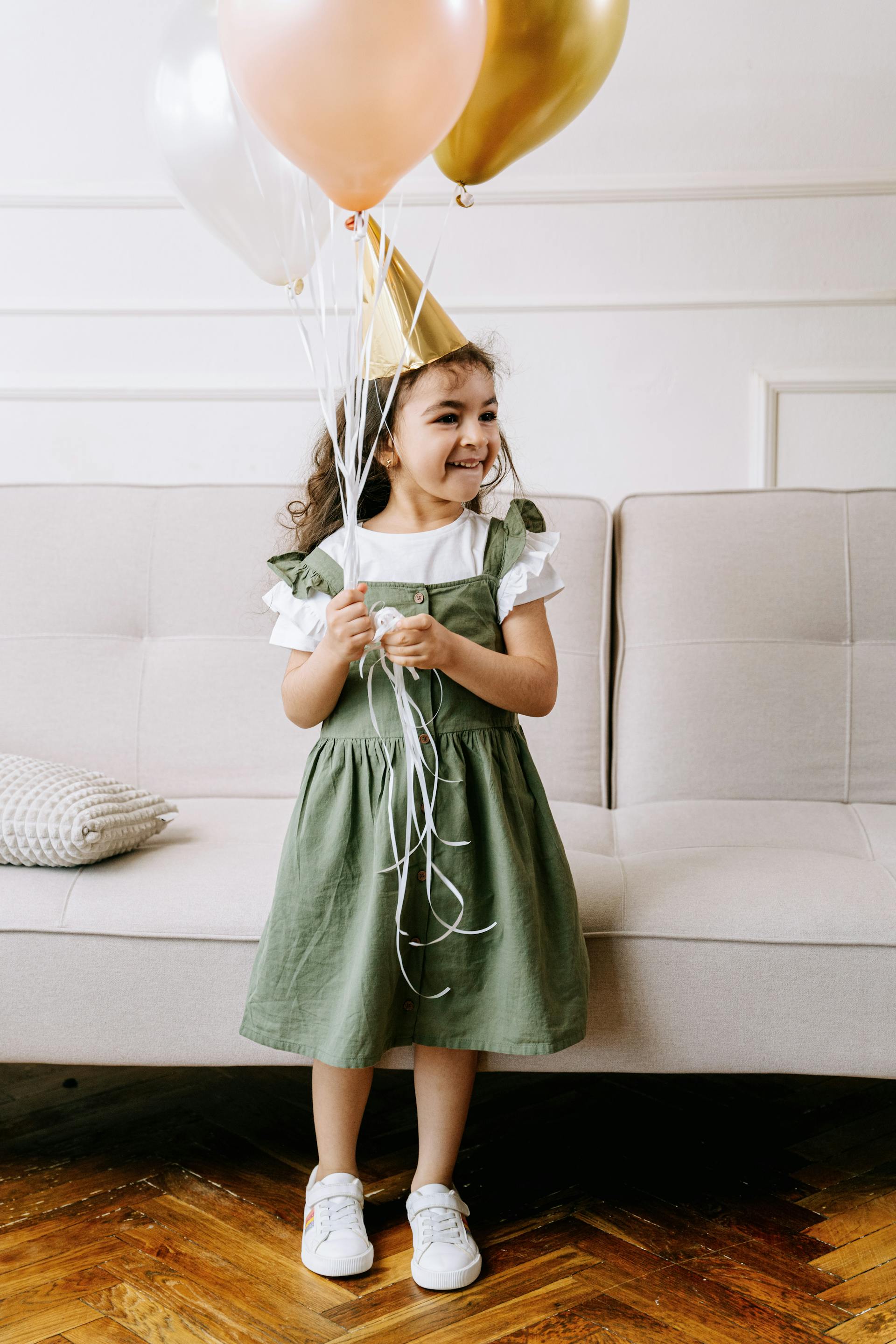 Une petite fille portant un chapeau de fête tout en tenant des ballons | Source : Pexels