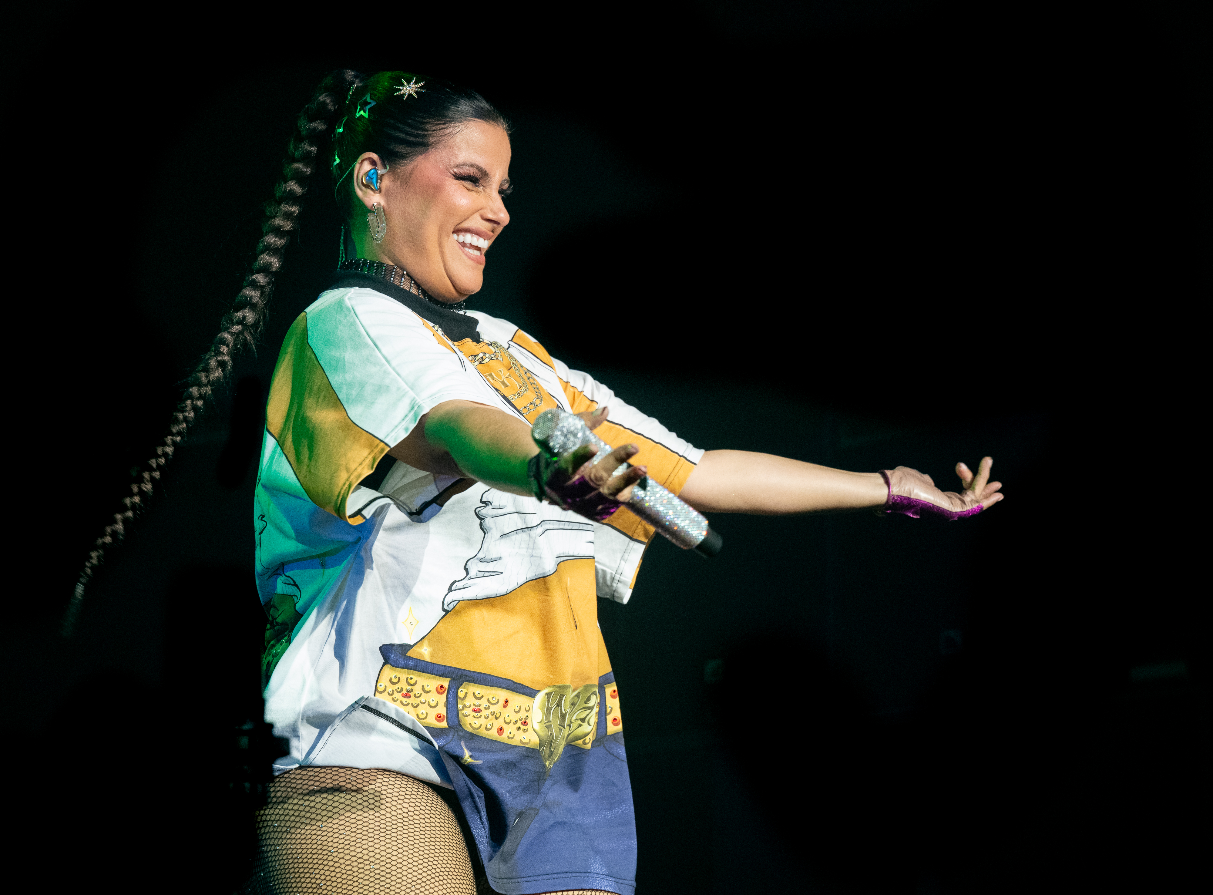 Furtado se produit sur scène vêtue d'un t-shirt graphique au motif inspiré d'une ceinture, associé à un short et des bas résille. Elle porte ses cheveux en longue tresse et accessoirise sa tenue avec des boucles d'oreilles, un collier ras-du-cou et un maquillage audacieux. Elle tient un micro dans une main et fait des gestes à la foule de l'autre.