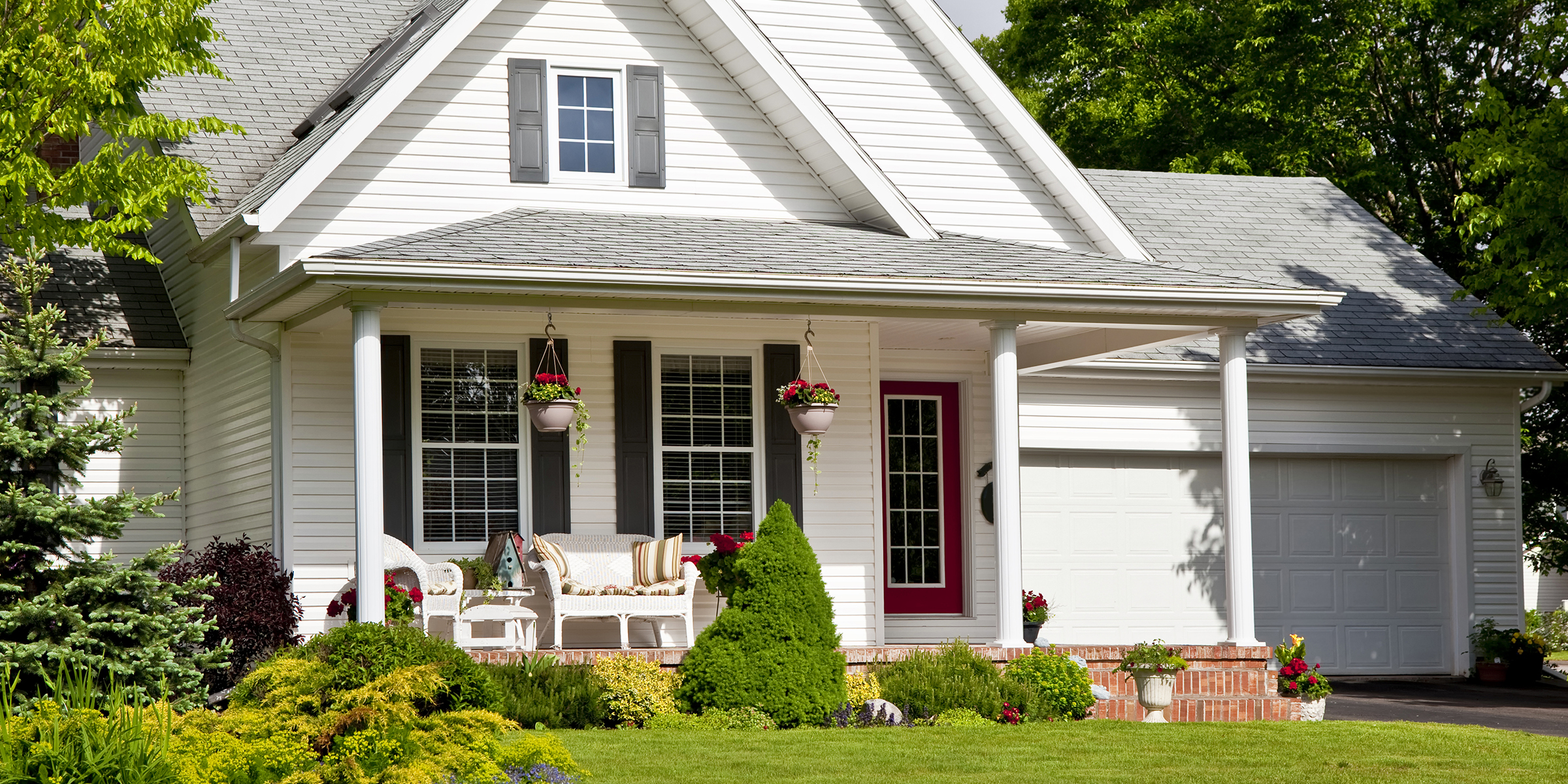 Une charmante maison de banlieue avec une porte d'entrée rouge, des sièges de porche confortables et un aménagement paysager vibrant en pleine floraison | Source : Shutterstock