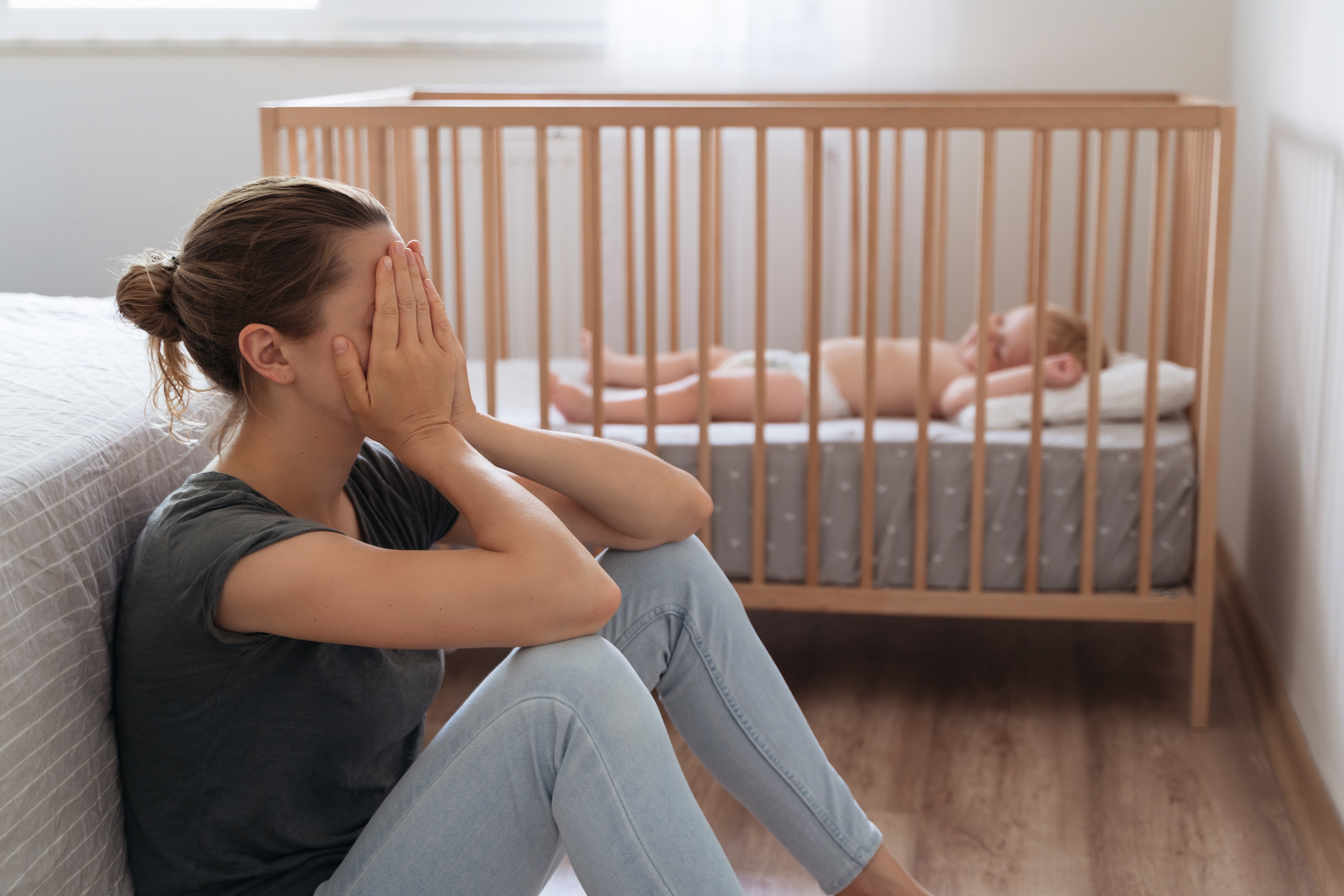 Une fille en détresse assise sur le sol alors qu'un bébé dort sur un berceau à proximité | Source : Shutterstock