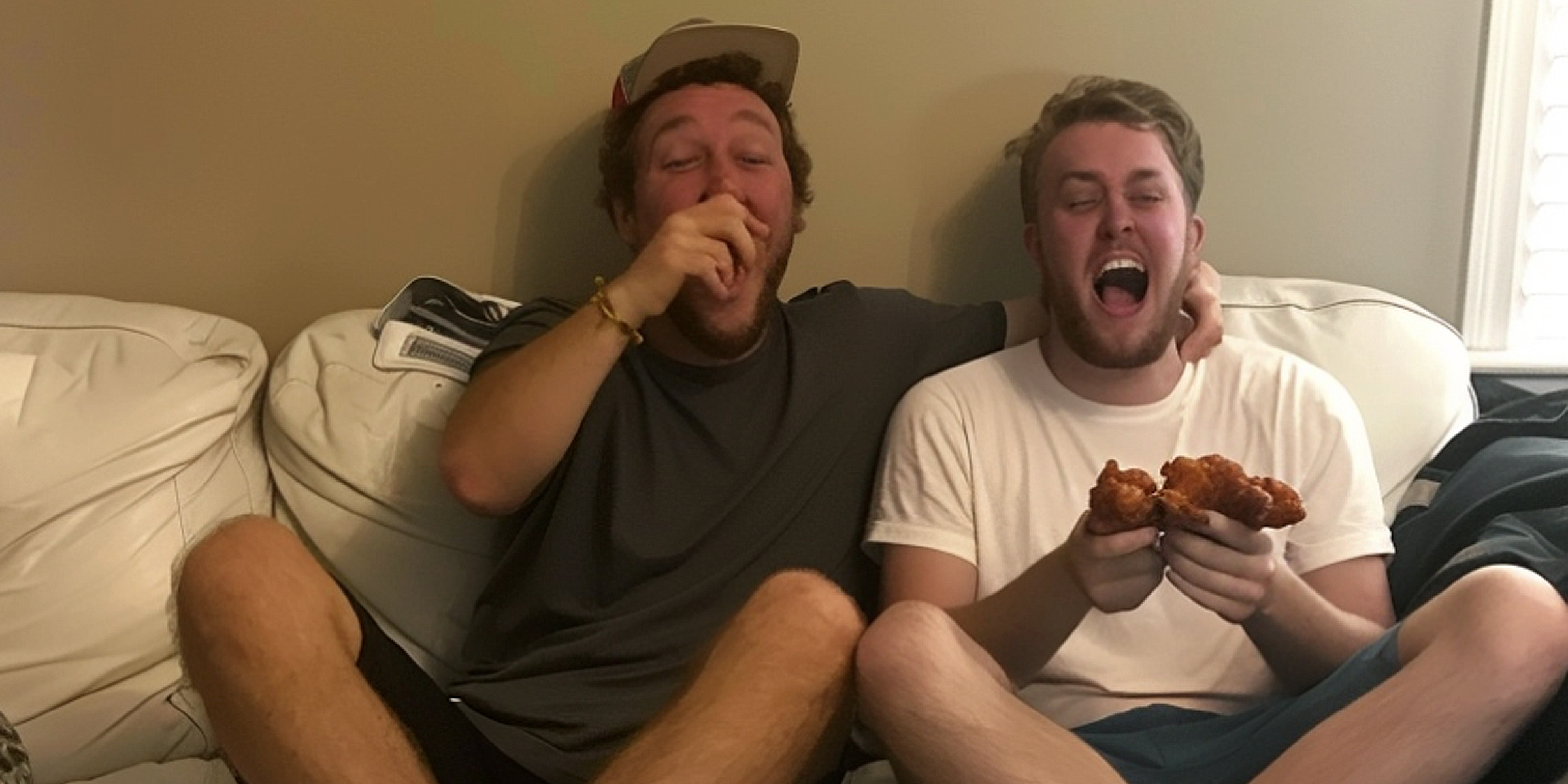 Deux hommes qui mangent et rient sur un canapé | Source : Ozdomedia