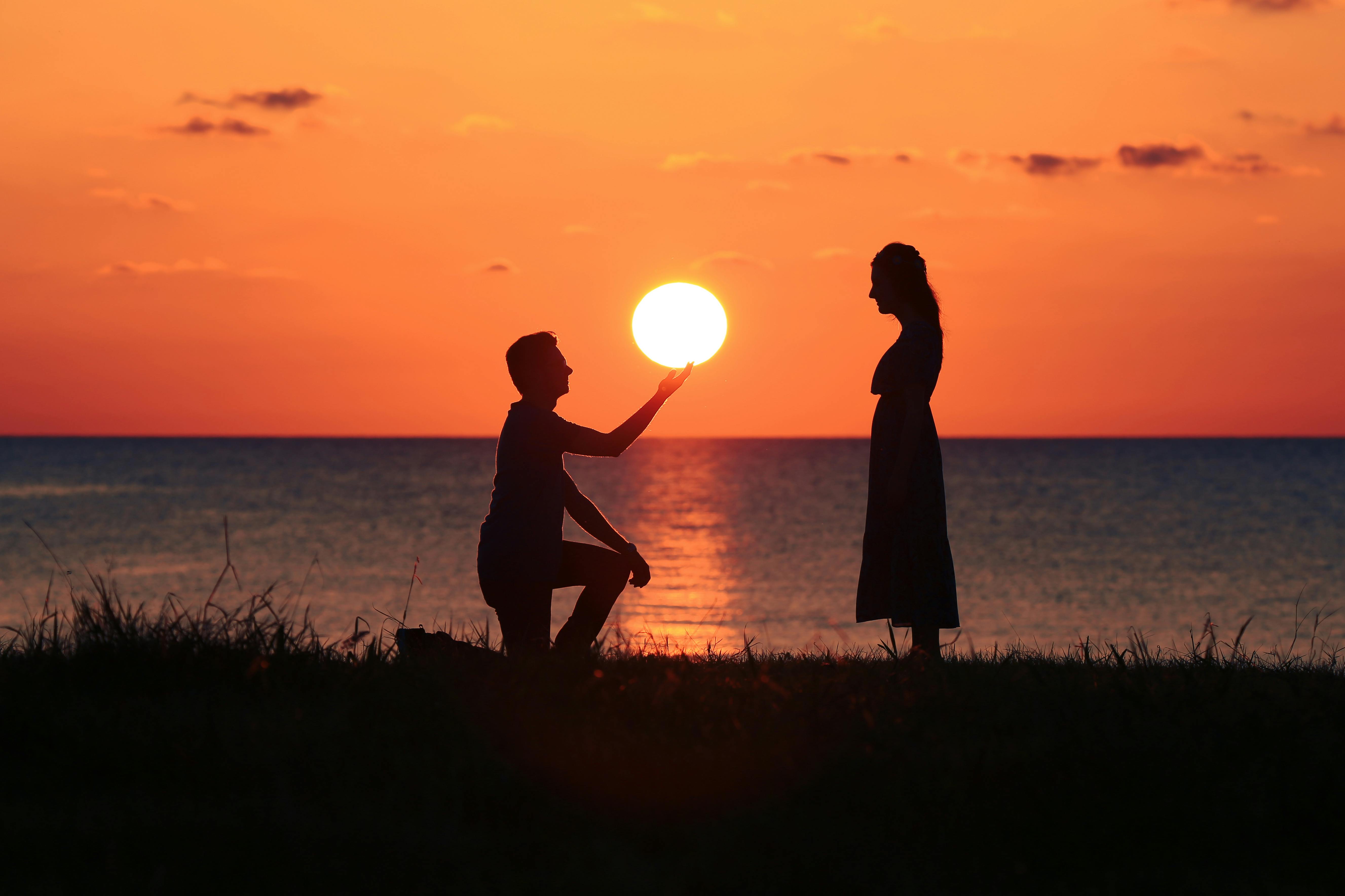 Silhouette d'un homme agenouillé devant une femme au coucher du soleil | Source : Pexels