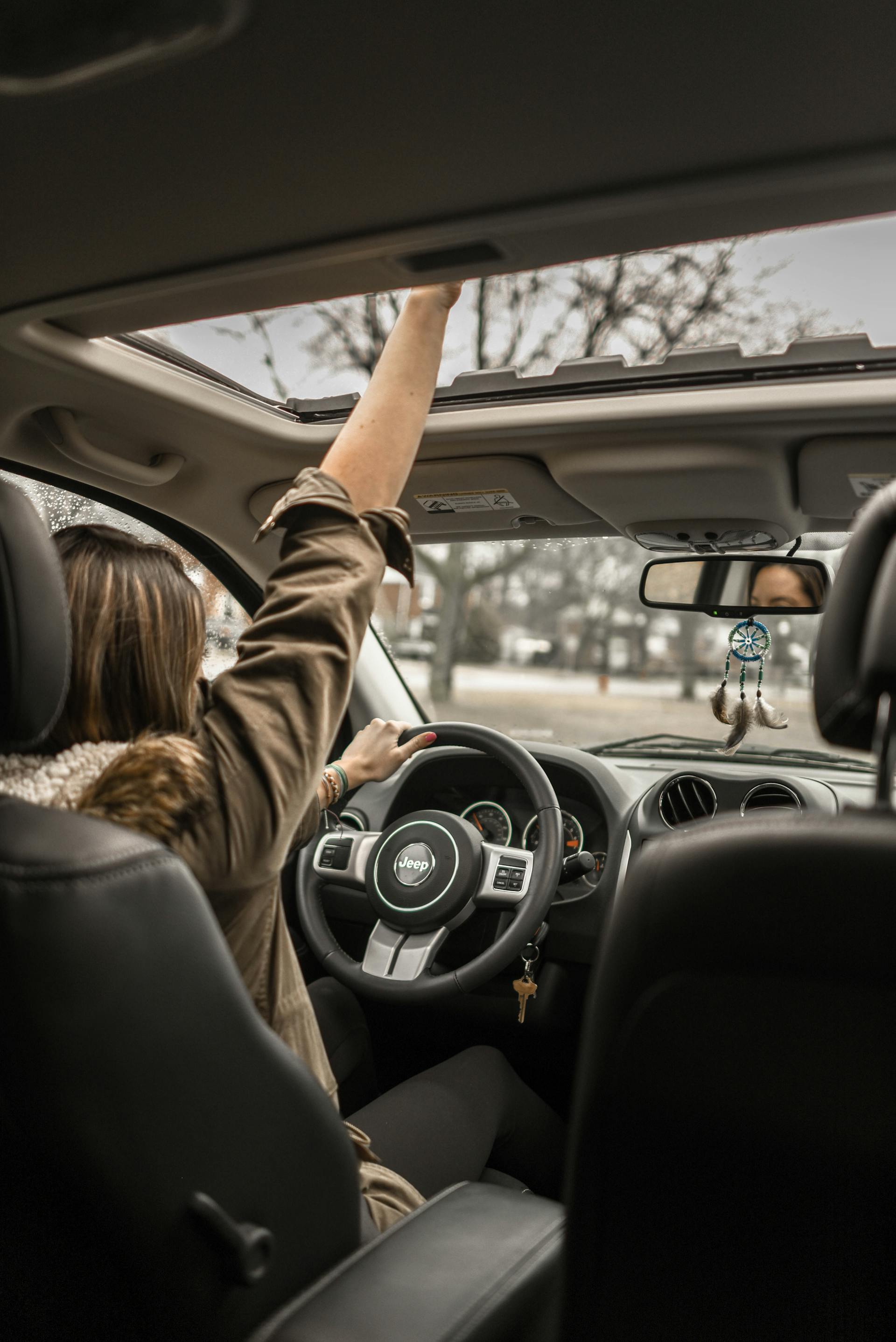 Une femme fait un signe de la main à travers le toit ouvrant d'une voiture | Source : Pexels