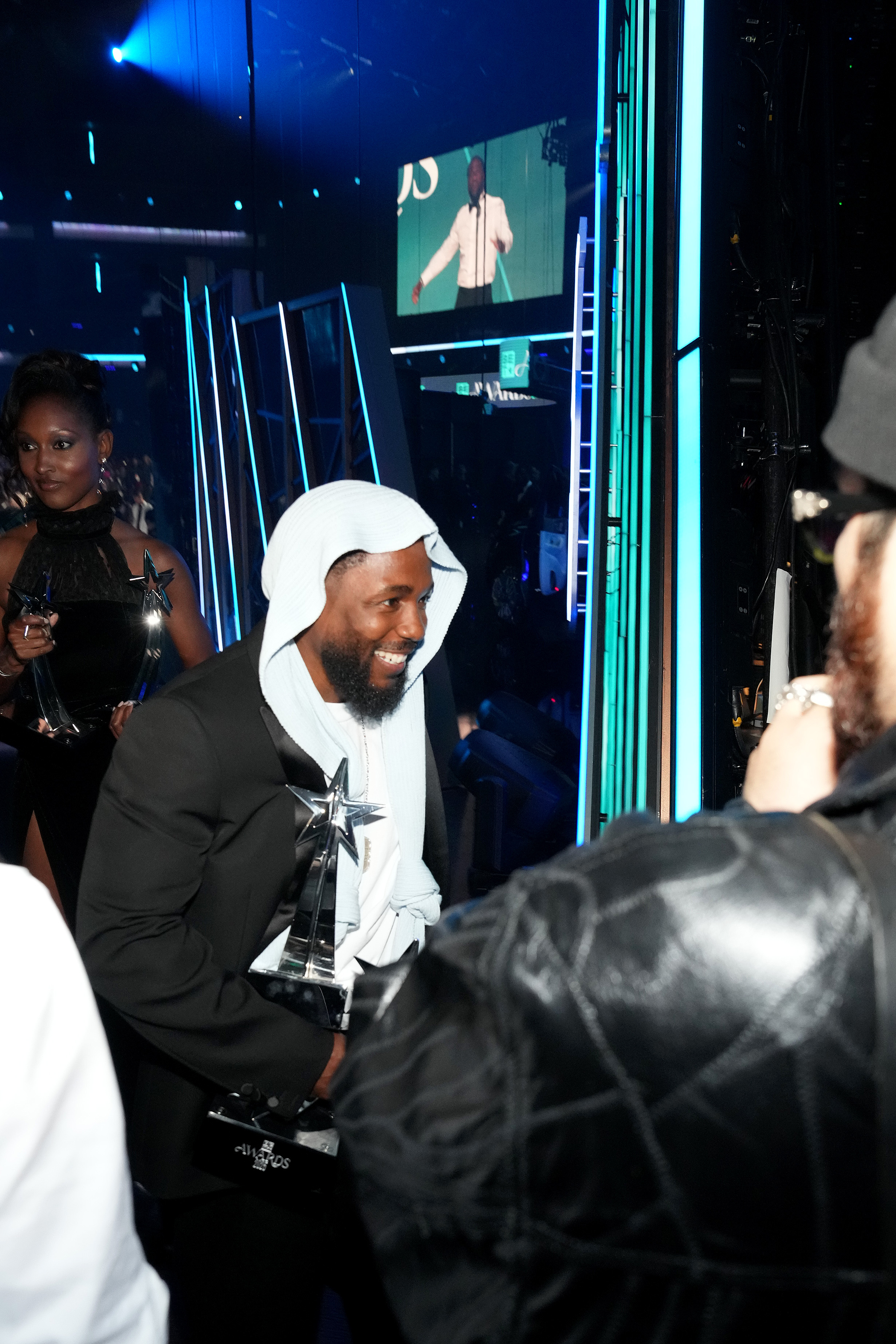 Dans les coulisses du Peacock Theater, Kendrick Lamar est tout sourire alors qu'il salue les sympathisants et s'agrippe à plusieurs prix après ses victoires aux BET Awards 2025. Son look superposé comprenait une coiffe en tricot nouée sur le devant.