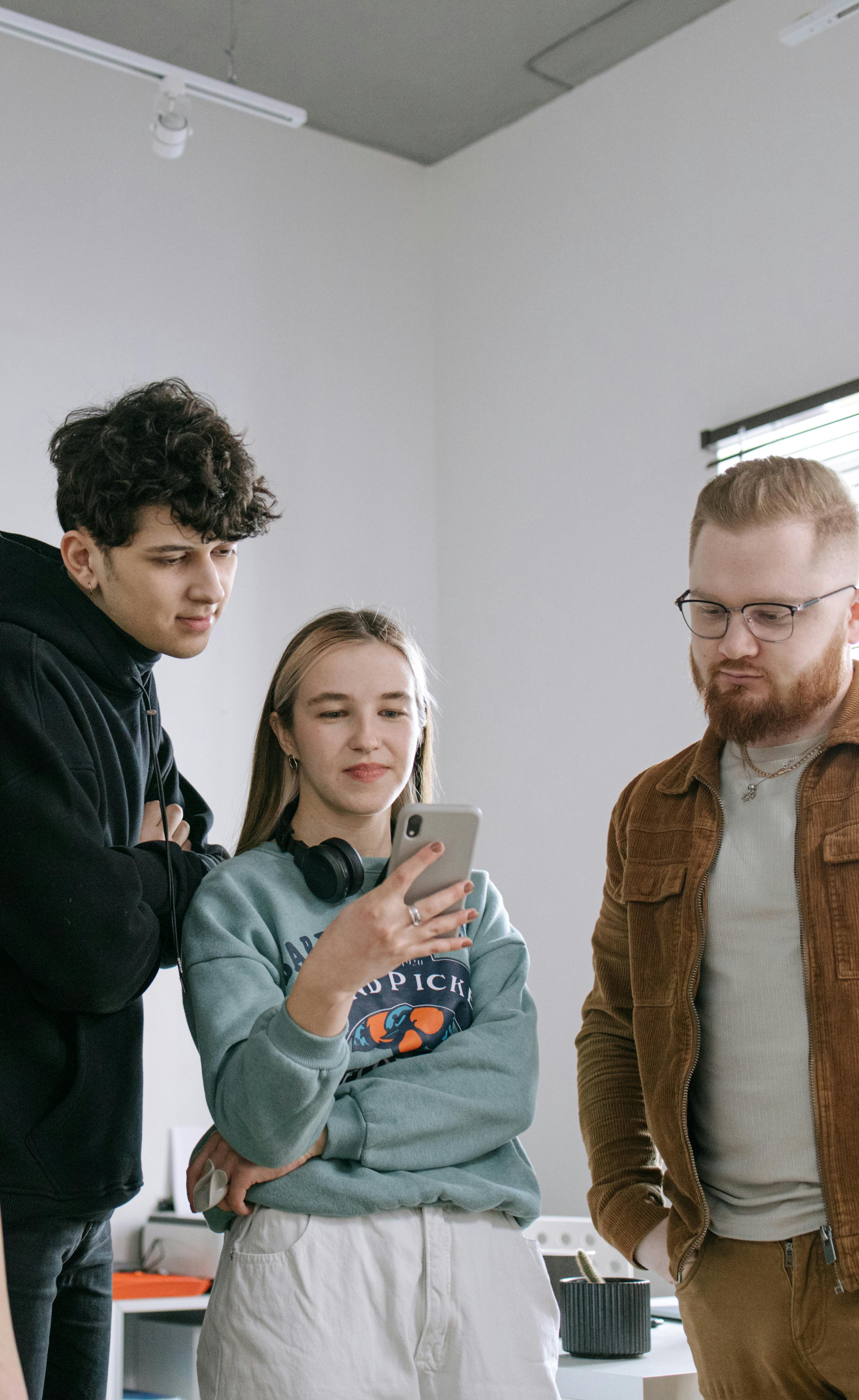 Une femme et deux hommes regardent un téléphone tout en complotant quelque chose | Source : Pexels