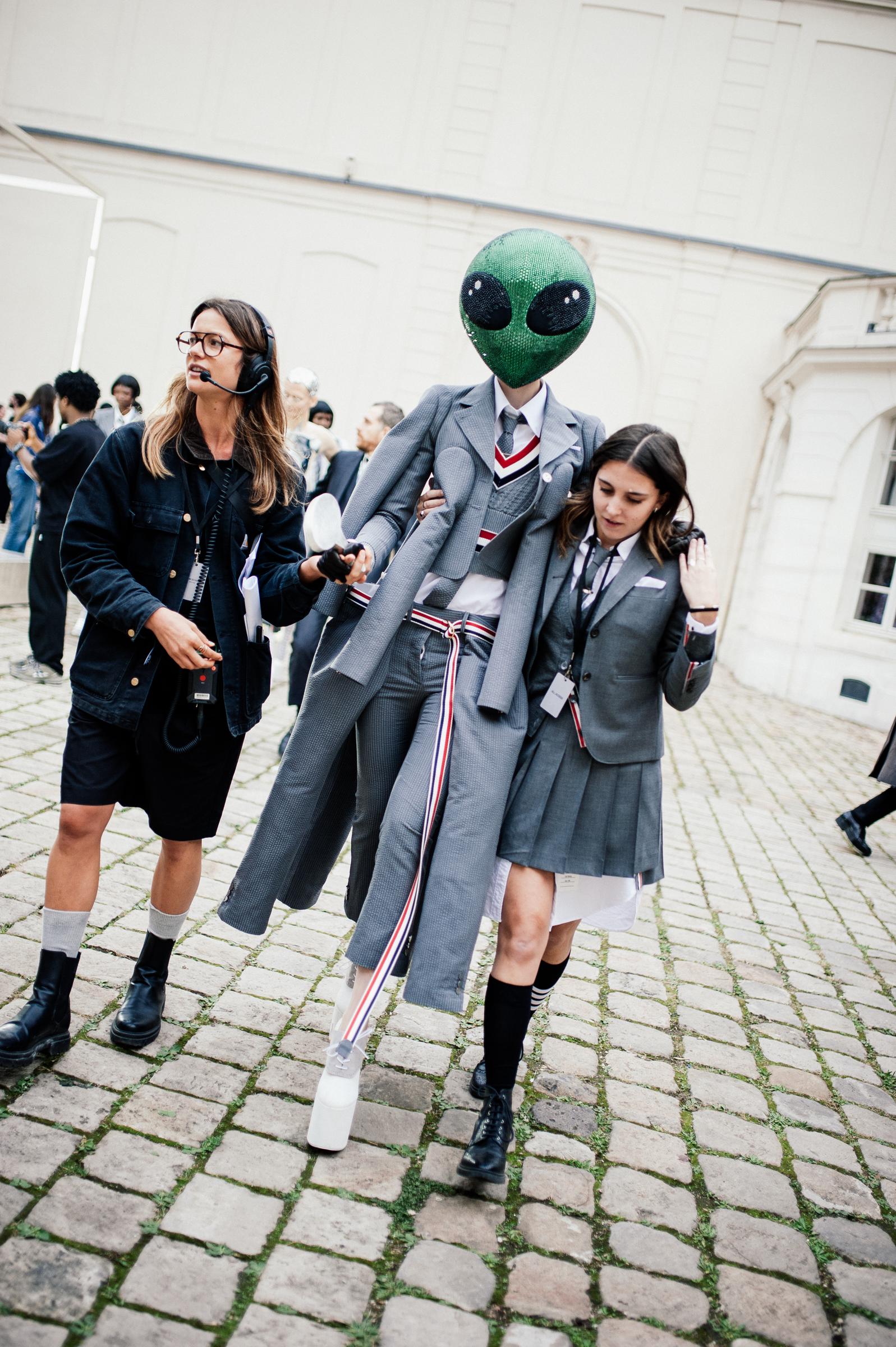 Un look Thom Browne est présenté en coulisses lors de la Fashion Week printemps/été 2026 à Paris, en France. Le mannequin porte un couvre-chef vert extraterrestre associé à un costume classique en flanelle grise. Il est transformé par six manches et autant de jambes pour un effet saisissant et surréaliste.