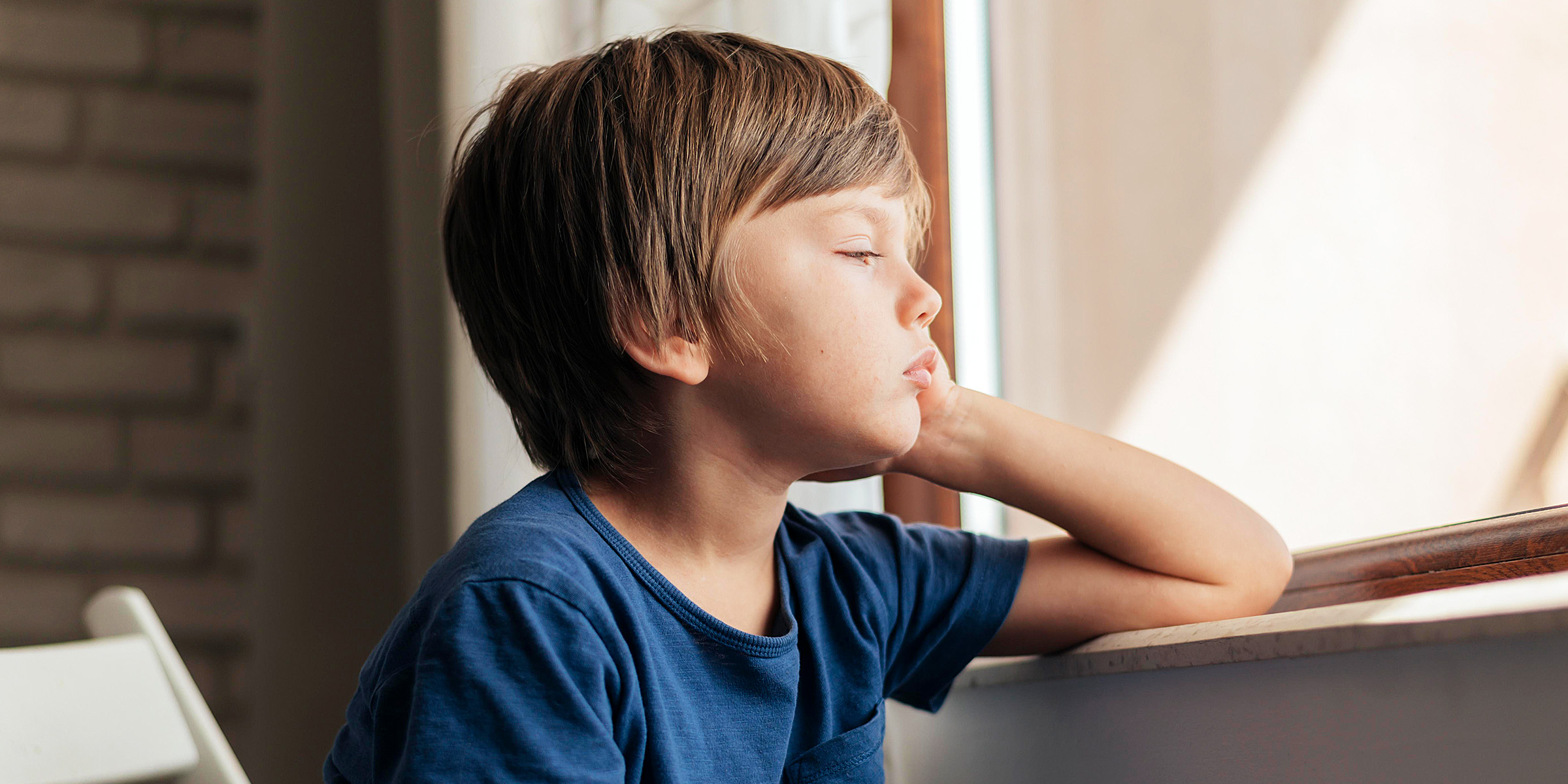 Un petit garçon triste assis près d'une fenêtre | Source : Freepik