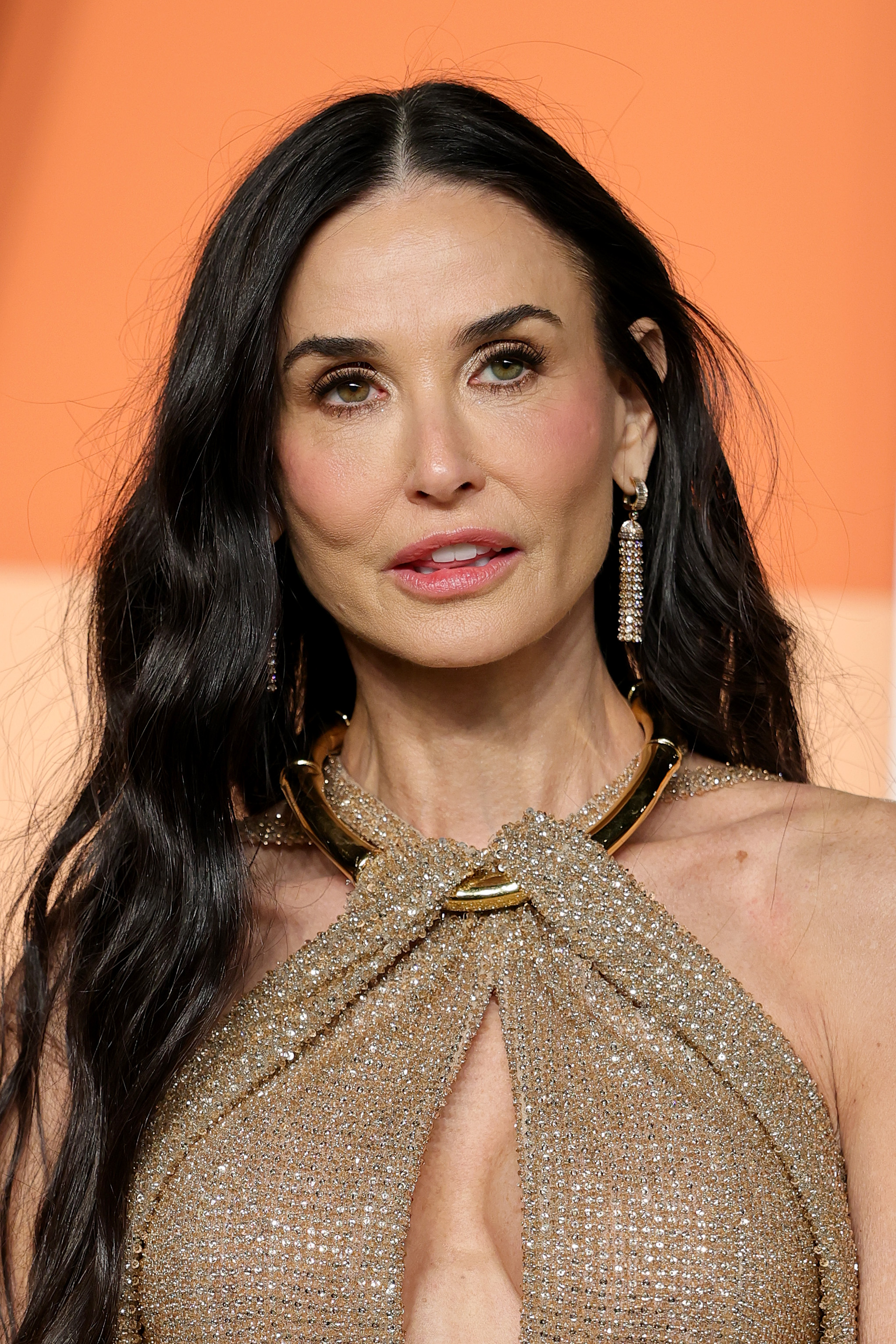 Demi Moore assiste à la Vanity Fair Oscar Party 2025 organisée par Radhika Jones au Wallis Annenberg Center for the Performing Arts le 2 mars 2025 à Beverly Hills, en Californie. L'actrice a coiffé ses longs cheveux bruns ondulés avec une raie au milieu, associant ce look à une robe dos nu dorée scintillante et à des boucles d'oreilles imposantes.