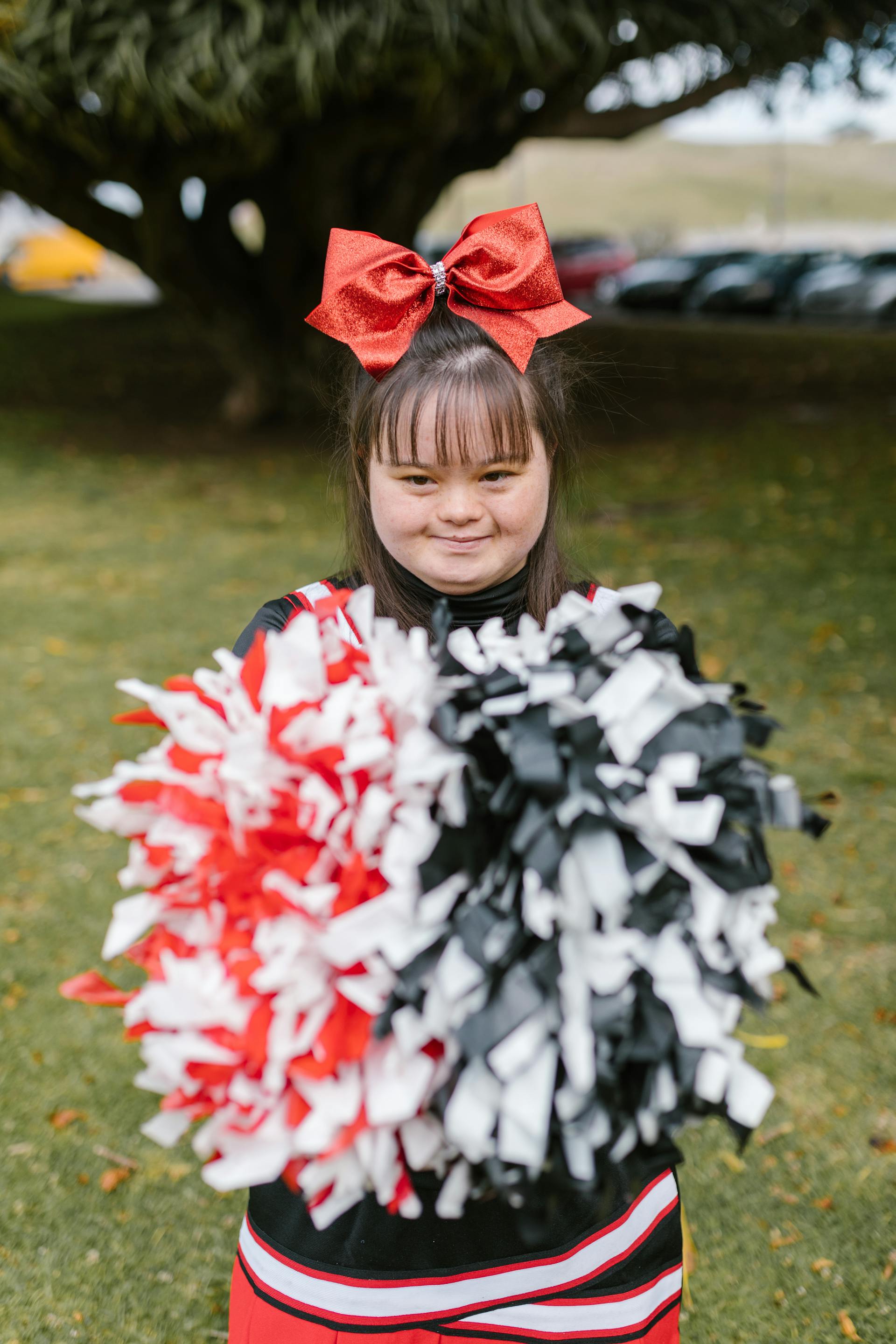 Une jeune fille atteinte du syndrome de Down en tenue de pom-pom girl et tenant des pompons | Source : Pexels