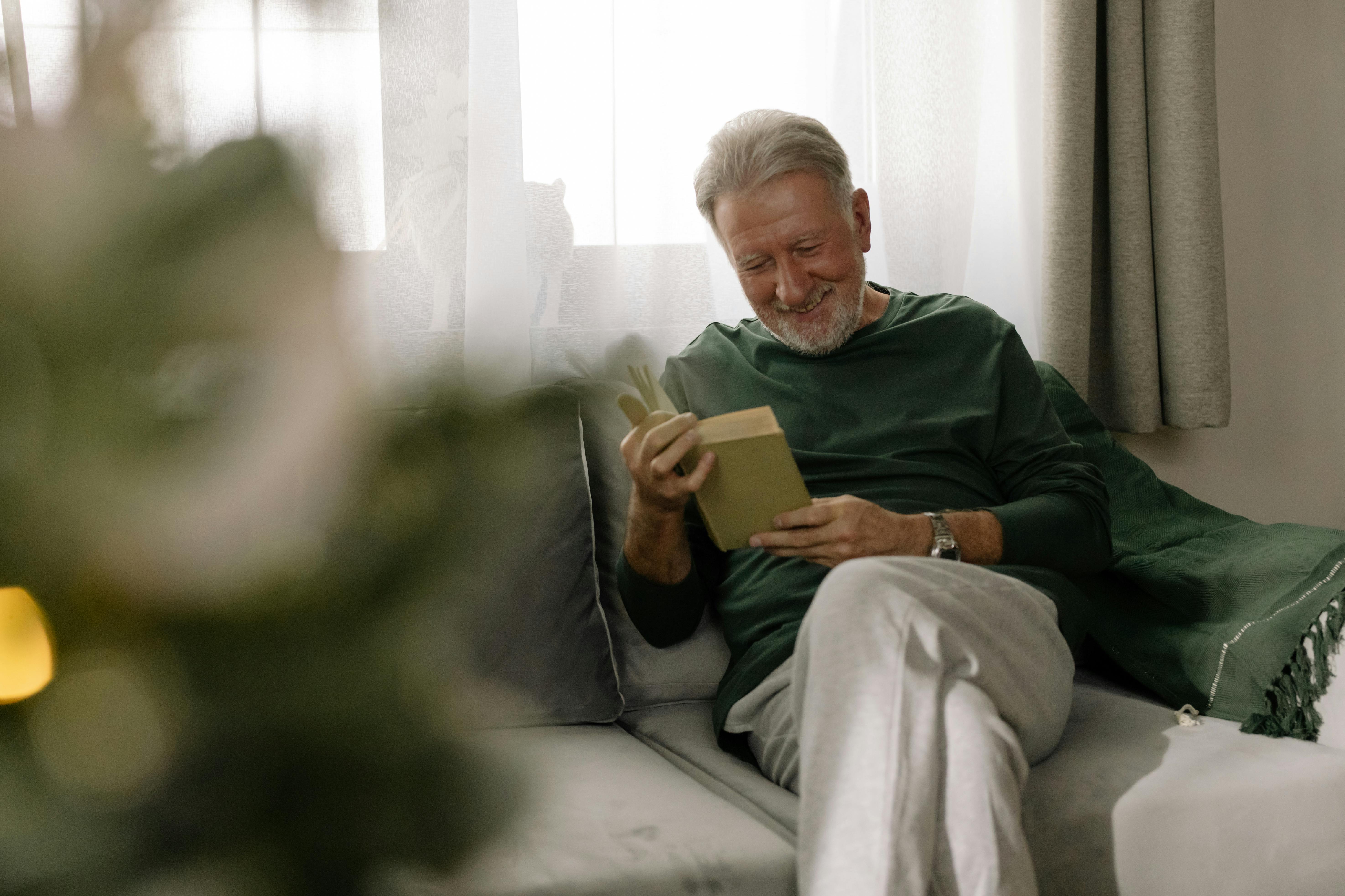 Un homme âgé souriant lisant un livre | Source : Pexels