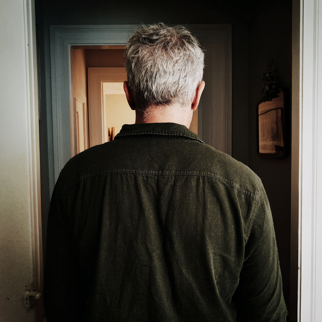 La vue arrière d'un homme âgé debout dans le couloir d'une maison | Source : Midjourney