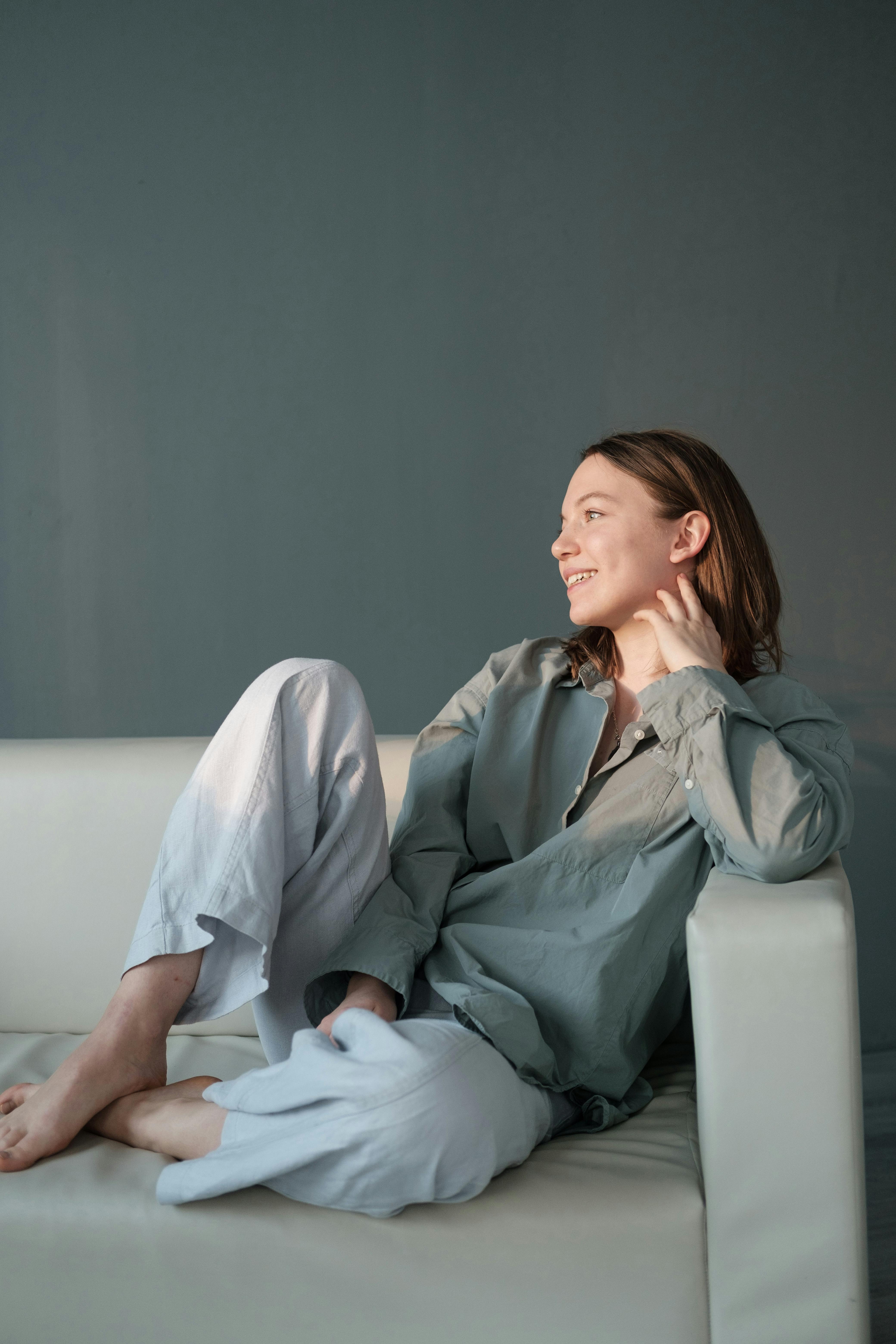 Femme souriante assise sur un canapé avec les jambes croisées | Source : Pexels