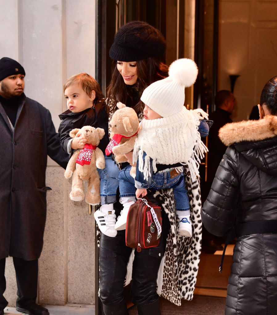 Amal Clooney sort avec des bottes à lacets et un manteau imprimé léopard, portant Alexander et Ella dans ses bras. La maman élégante concilie la mode et la famille alors que ses jumeaux s'accrochent à leurs jouets en peluche.