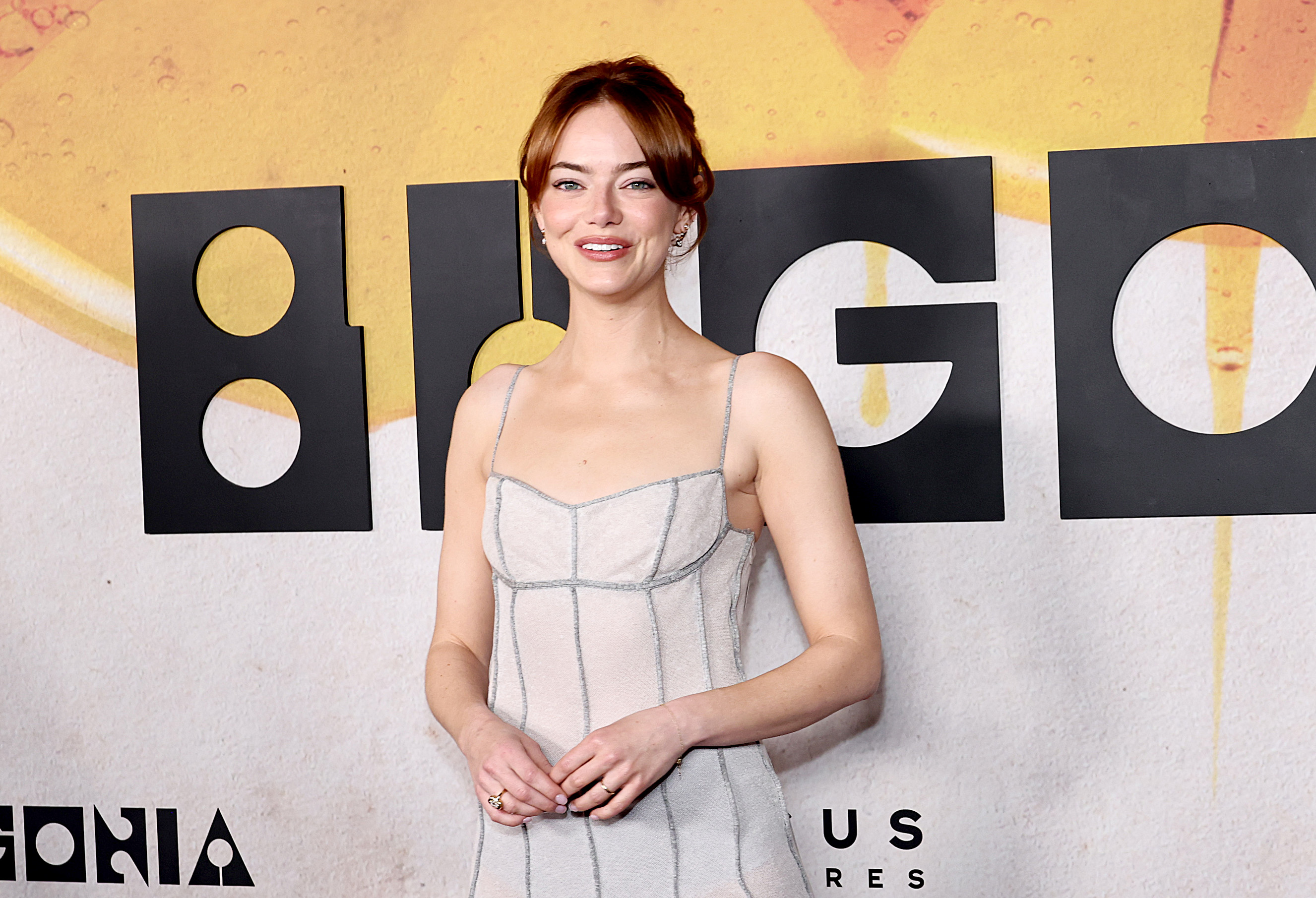 Emma Stone se tient debout devant la toile de fond « Bugonia », les épaules détendues, les yeux brillants sous les projecteurs — un équilibre entre élégance moderne et assurance sereine.