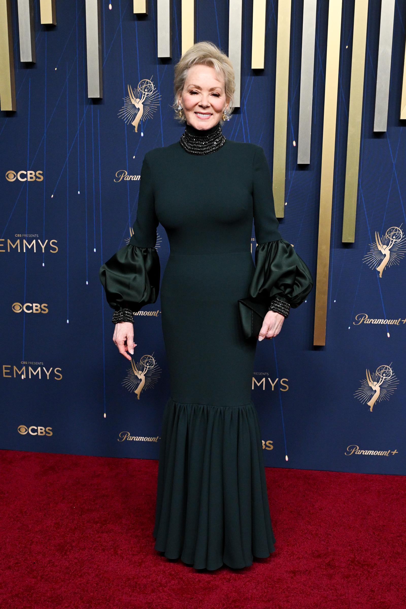 Jean Smart rayonne de majesté aux Emmys dans une robe vert forêt moulante à manches bouffantes et col montant. Les perles qui ornent le col et les poignets ajoutent une touche dramatique à sa tenue.