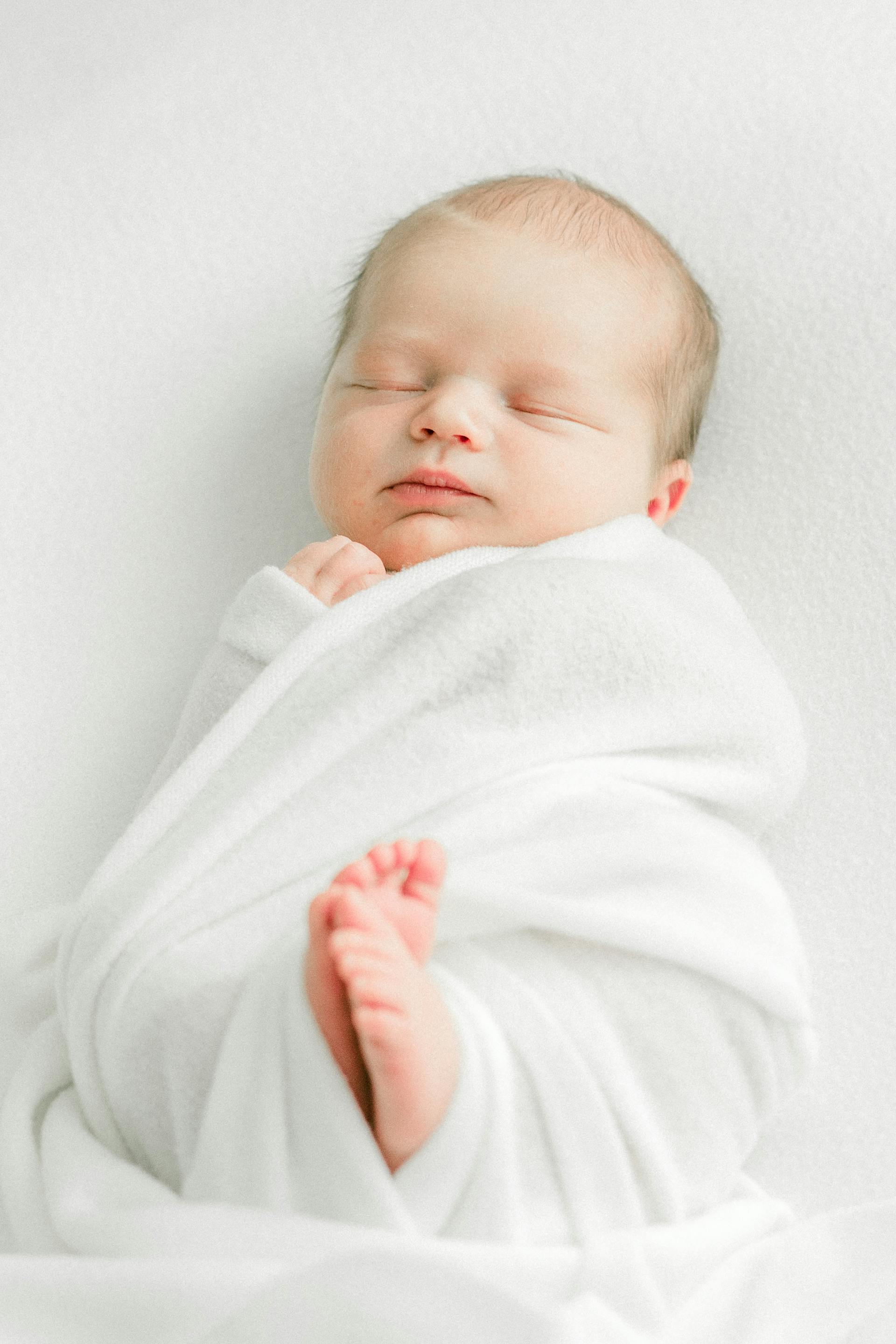 Un nouveau-né endormi enveloppé dans une couverture blanche | Source : Pexels