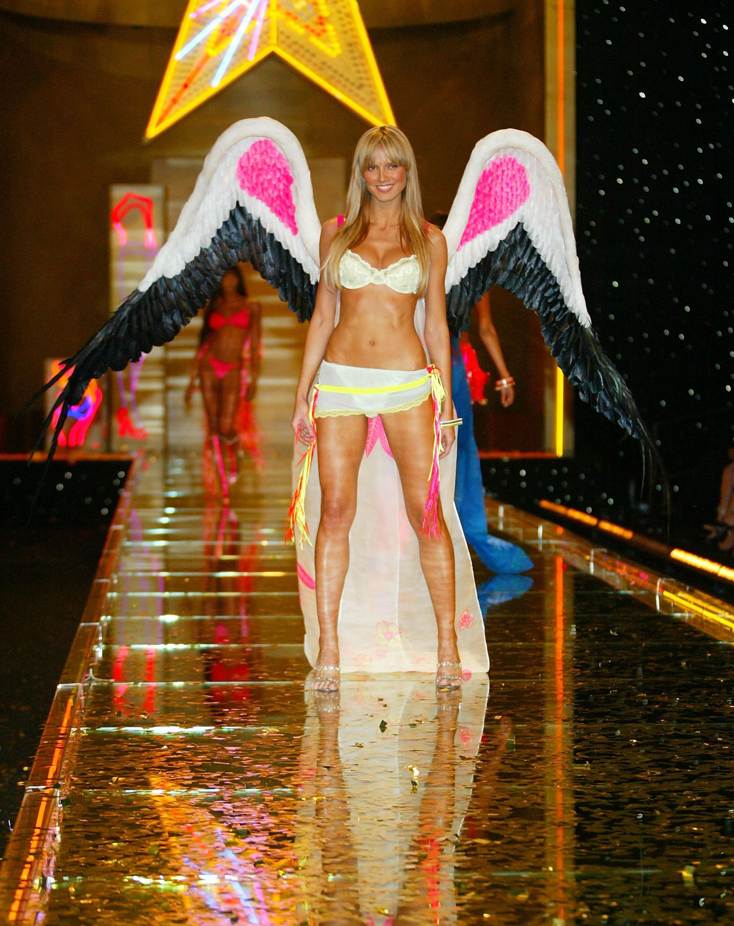 Heidi Klum porte un soutien-gorge en dentelle jaune avec un sarong floral transparent et des ailes aux accents roses et noirs lors du défilé de mode Victoria's Secret, le 14 novembre 2002, à l'armurerie de Lexington Avenue, à New York.