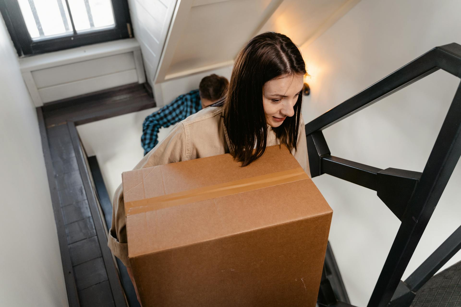 Une femme portant une boîte tout en montant les escaliers de sa maison | Source : Pexels