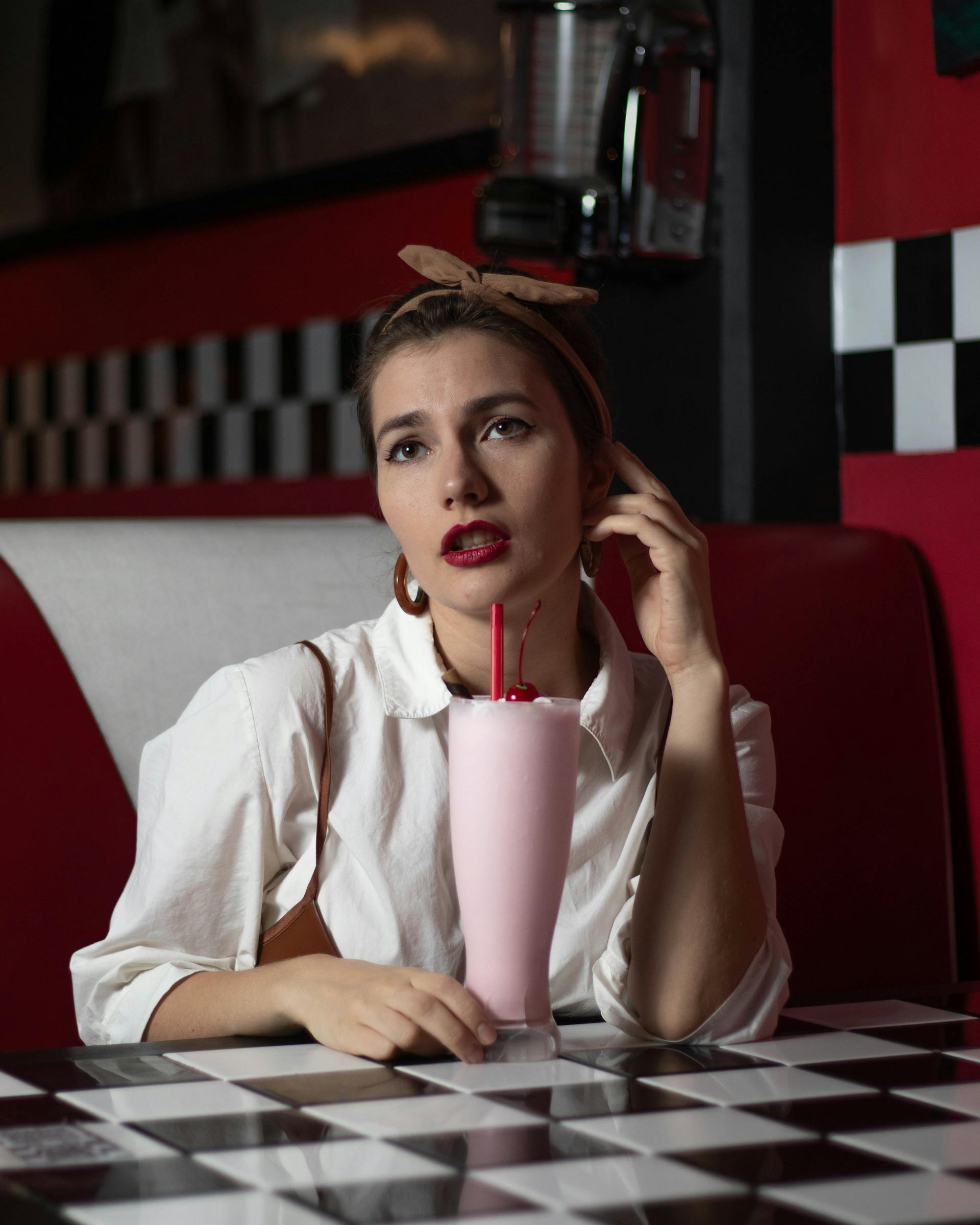 Une femme avec un verre de milkshake à la fraise assise dans un restaurant | Source : Pexels