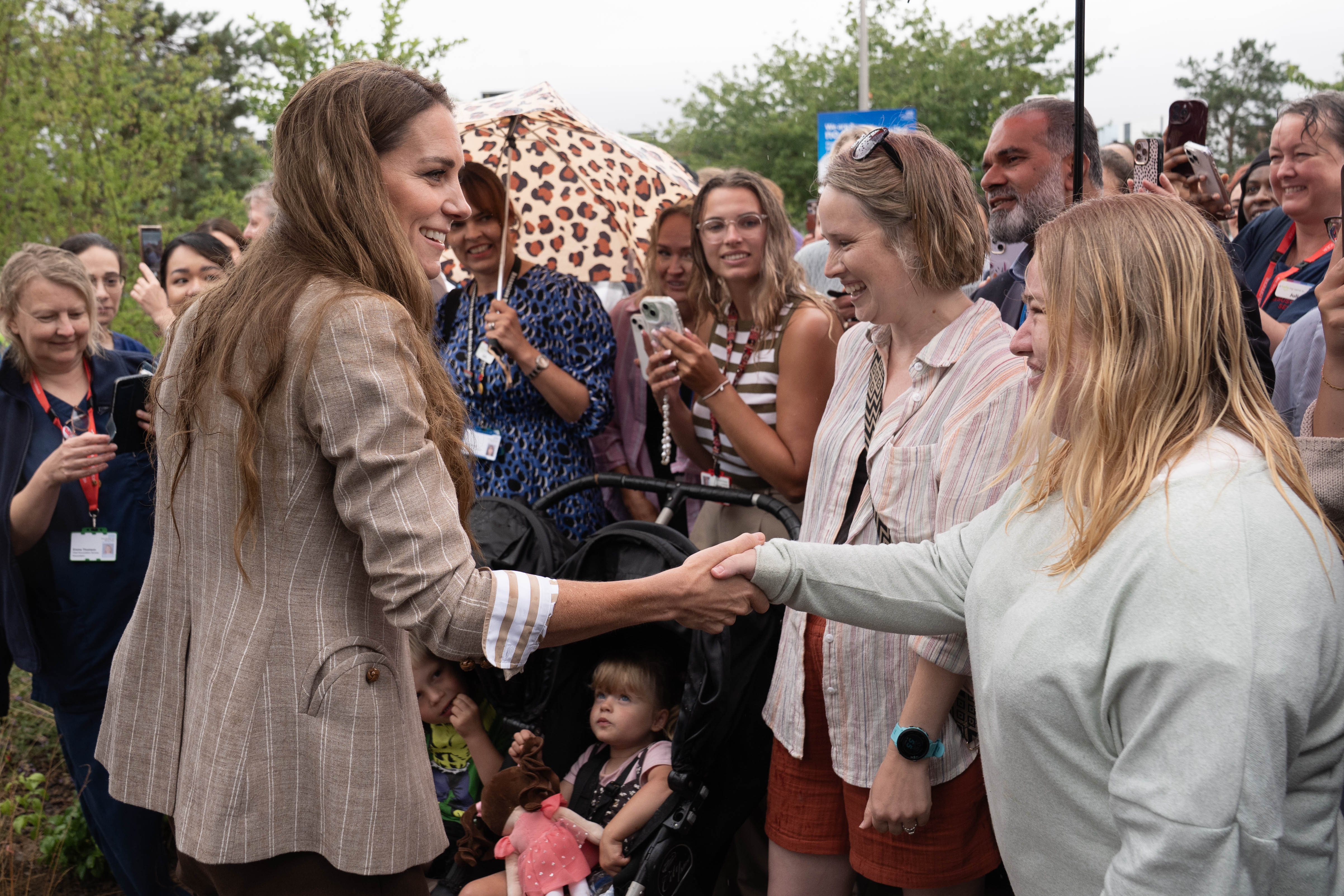 Dans un échange candide, la princesse Catherine salue les sympathisants d'une poignée de main et d'un sourire. La foule, y compris des enfants dans des poussettes, s'est rassemblée avec impatience pour rencontrer la princesse lors de son engagement public.