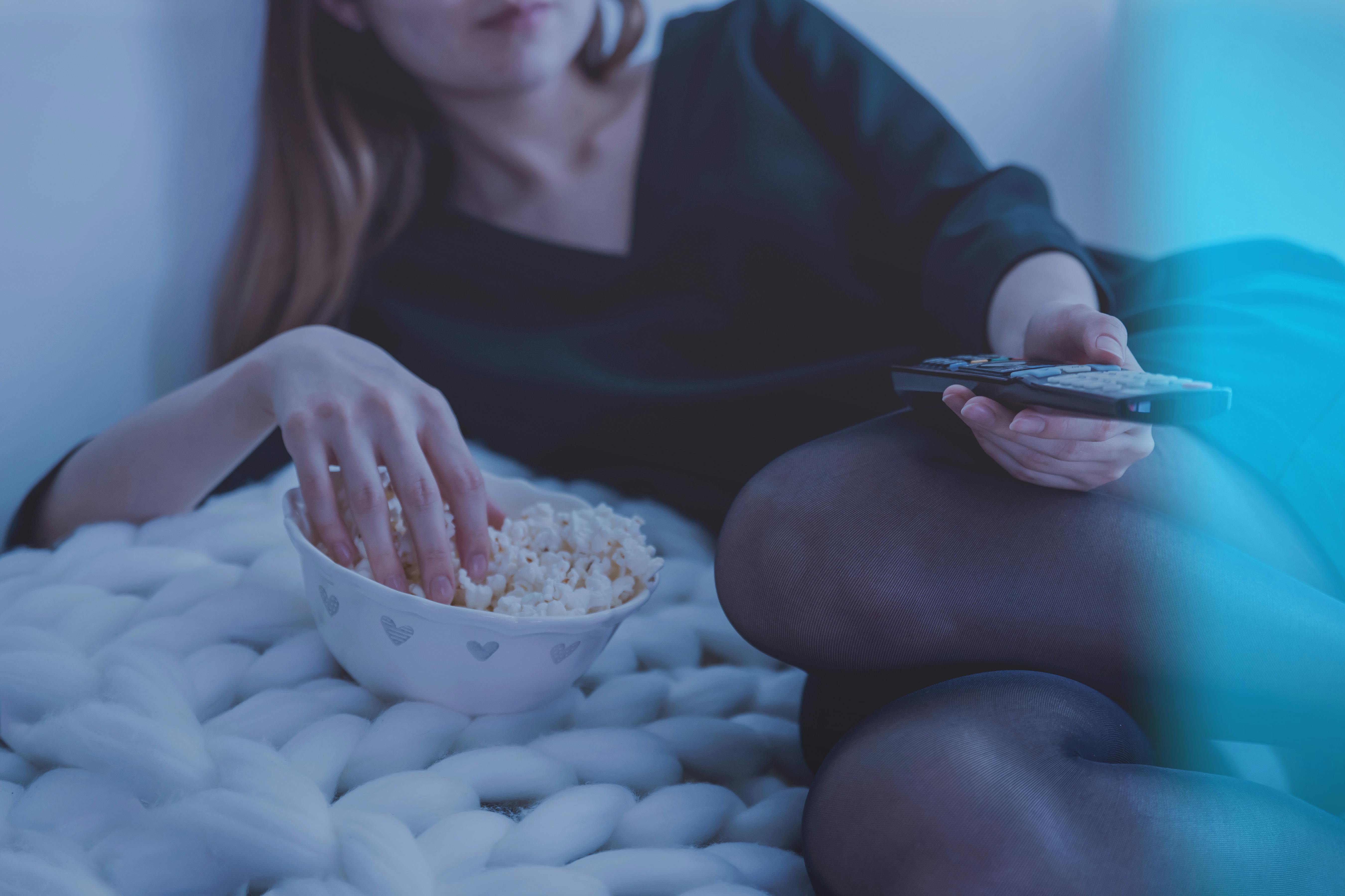 Une femme mangeant un bol de pop-corn et tenant une télécommande de télévision | Source : Pexels