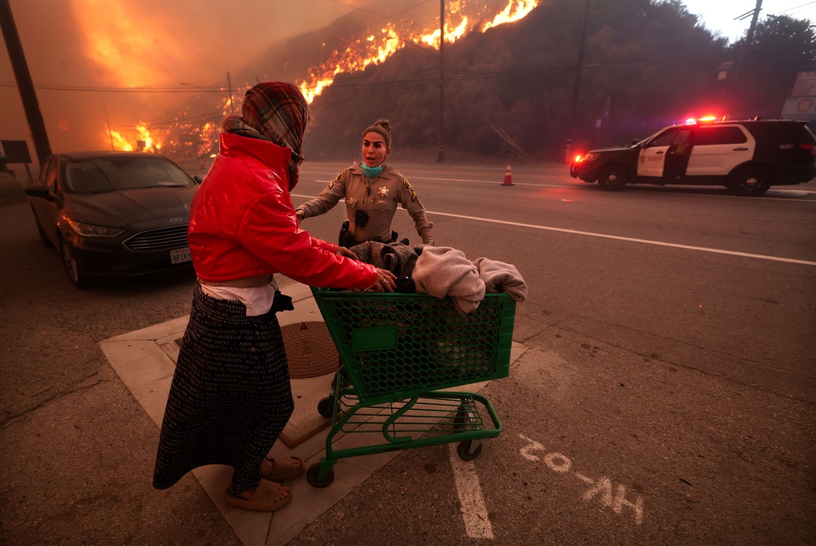 Un policier escortant une femme sans-abri loin de la Pacific Coast Highway et du Topanga Canyon Boulevard alors que l'incendie Palisades faisait rage dans les collines de Los Angeles, en Californie, le mardi 7 janvier 2025. | Source : Getty Images